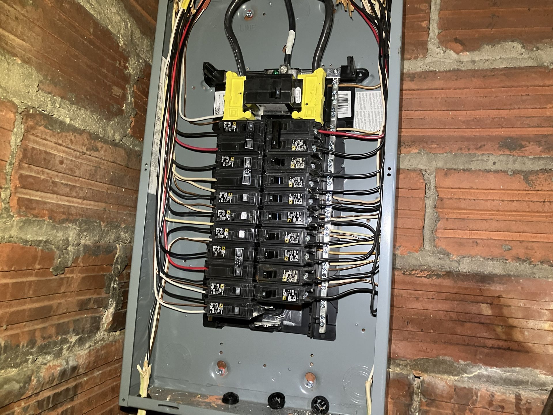 Open electrical breaker panel with multiple black switches and red, black, and white wires exposed