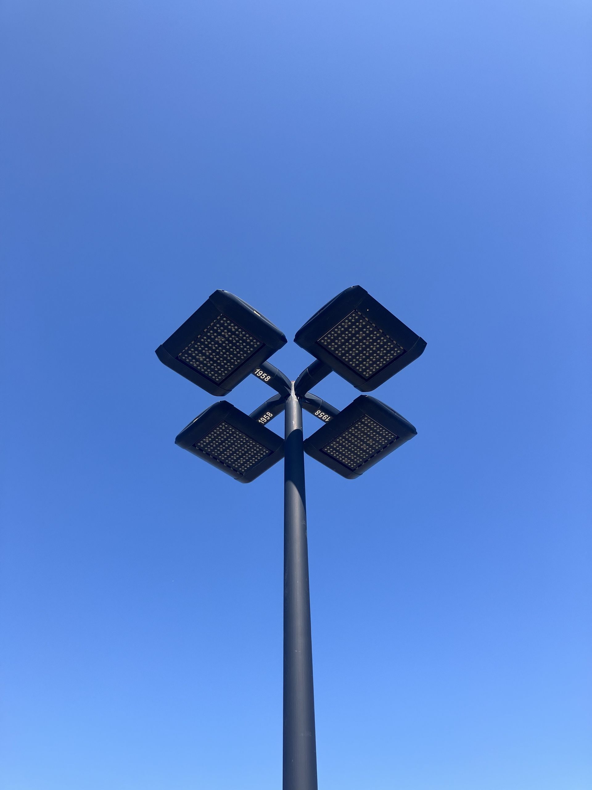 Four floodlights on a tall pole against a clear blue sky.