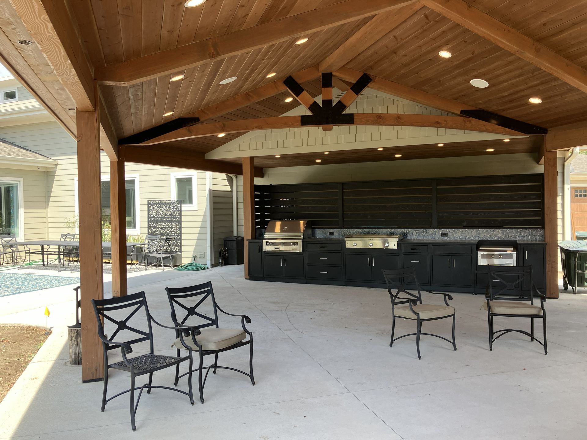 Covered outdoor patio with bar seating, ceiling fan, and black stools on a concrete floor.