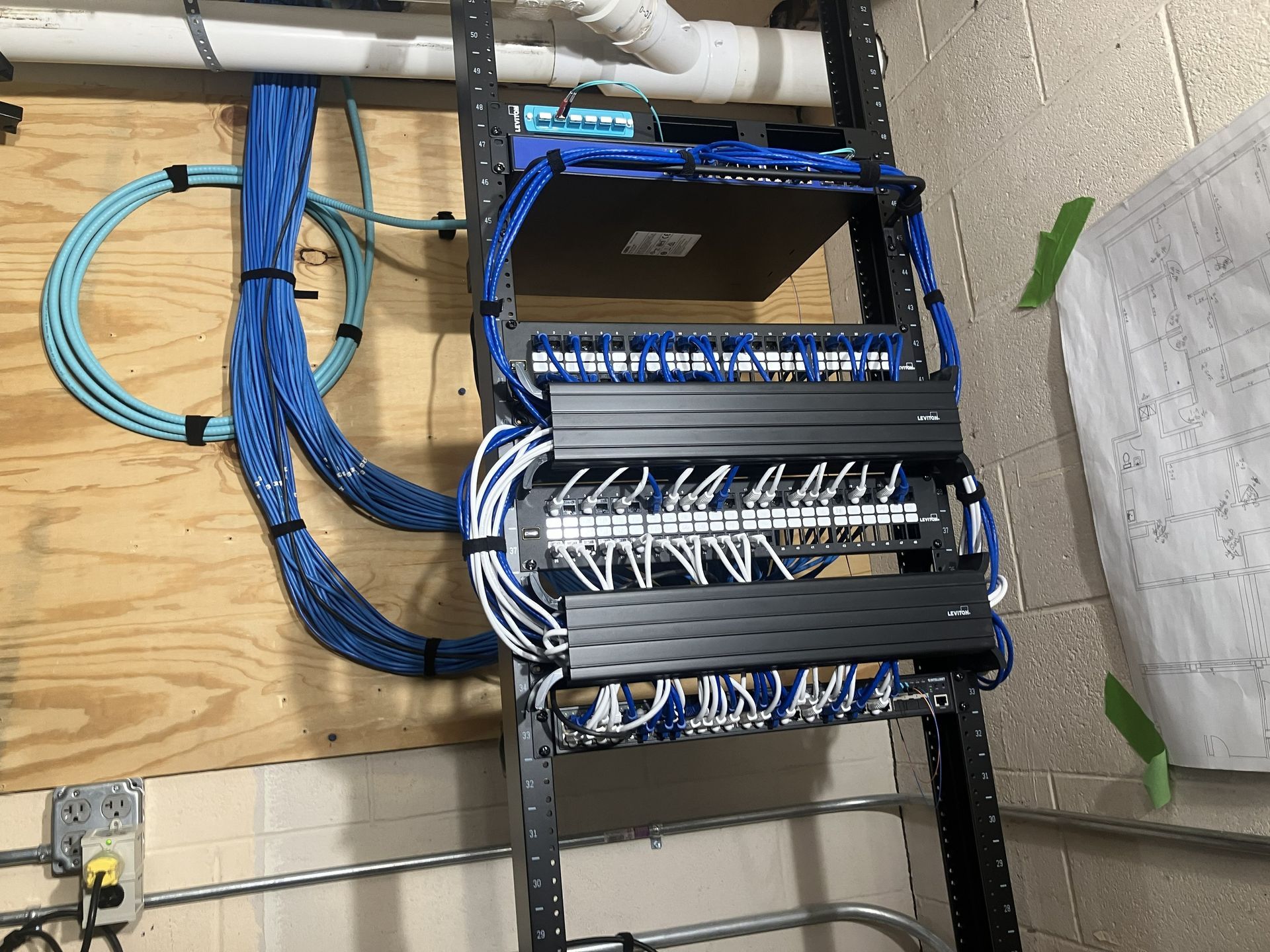 Network cables and patch panels in a wall-mounted rack in an unfinished utility room