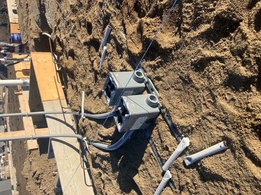 Electrical cable junction box buried in dirt beside a wooden formwork trench.