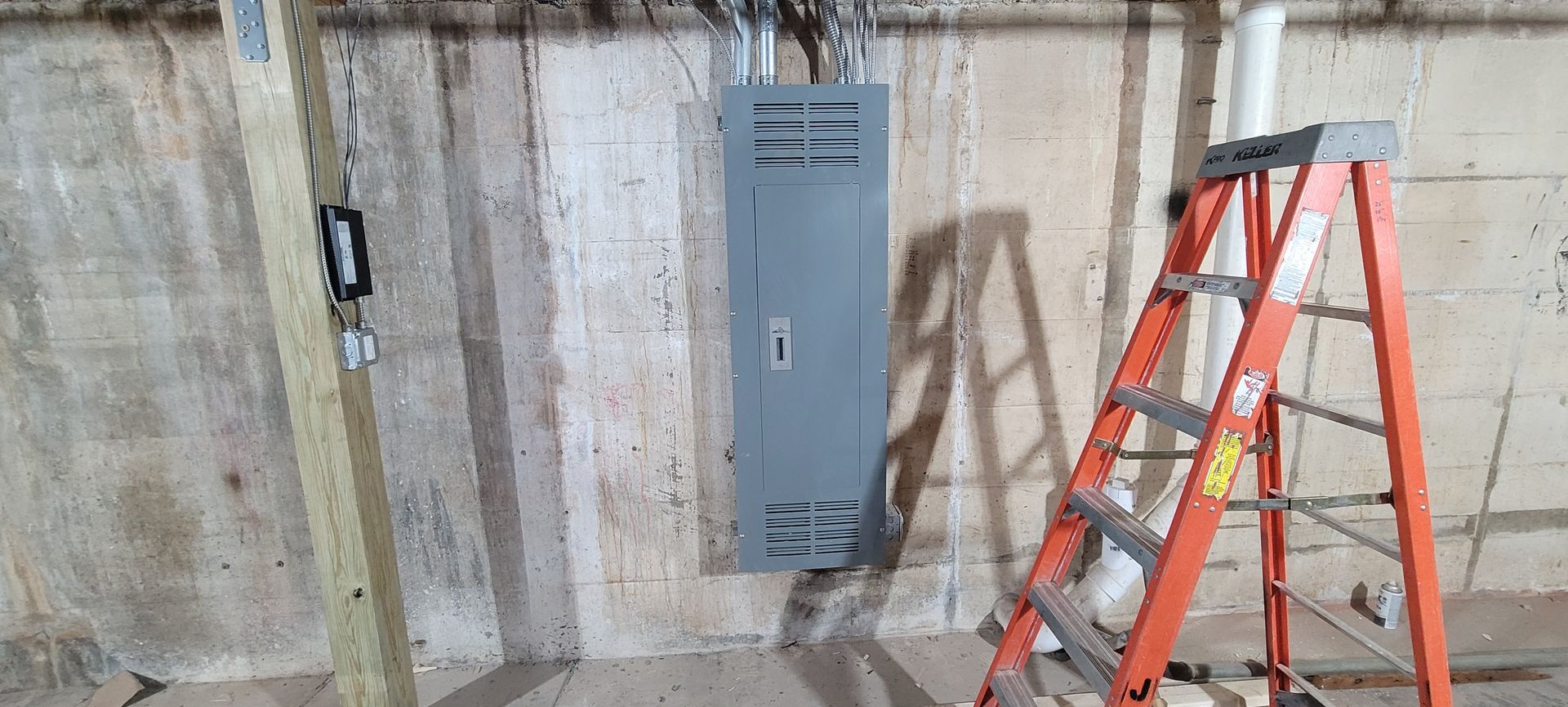 Basement wall with a gray metal panel and an orange ladder leaning nearby.