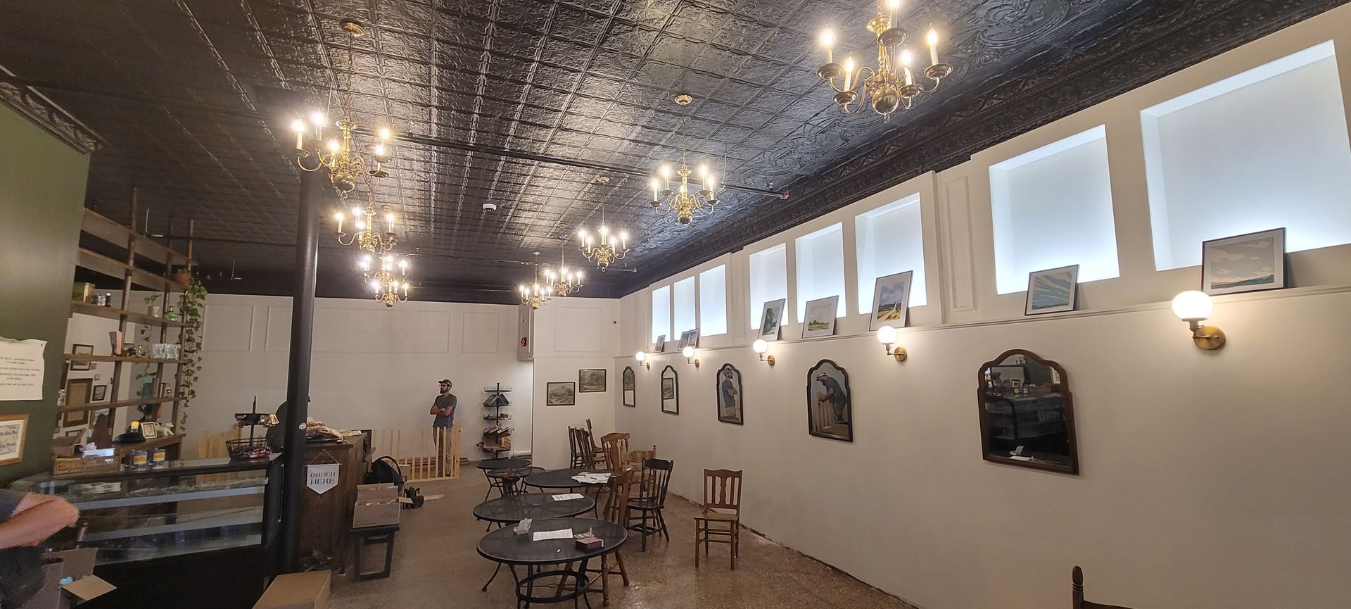 Modern café interior with ornate black ceiling, hanging lights, and tables by large windows