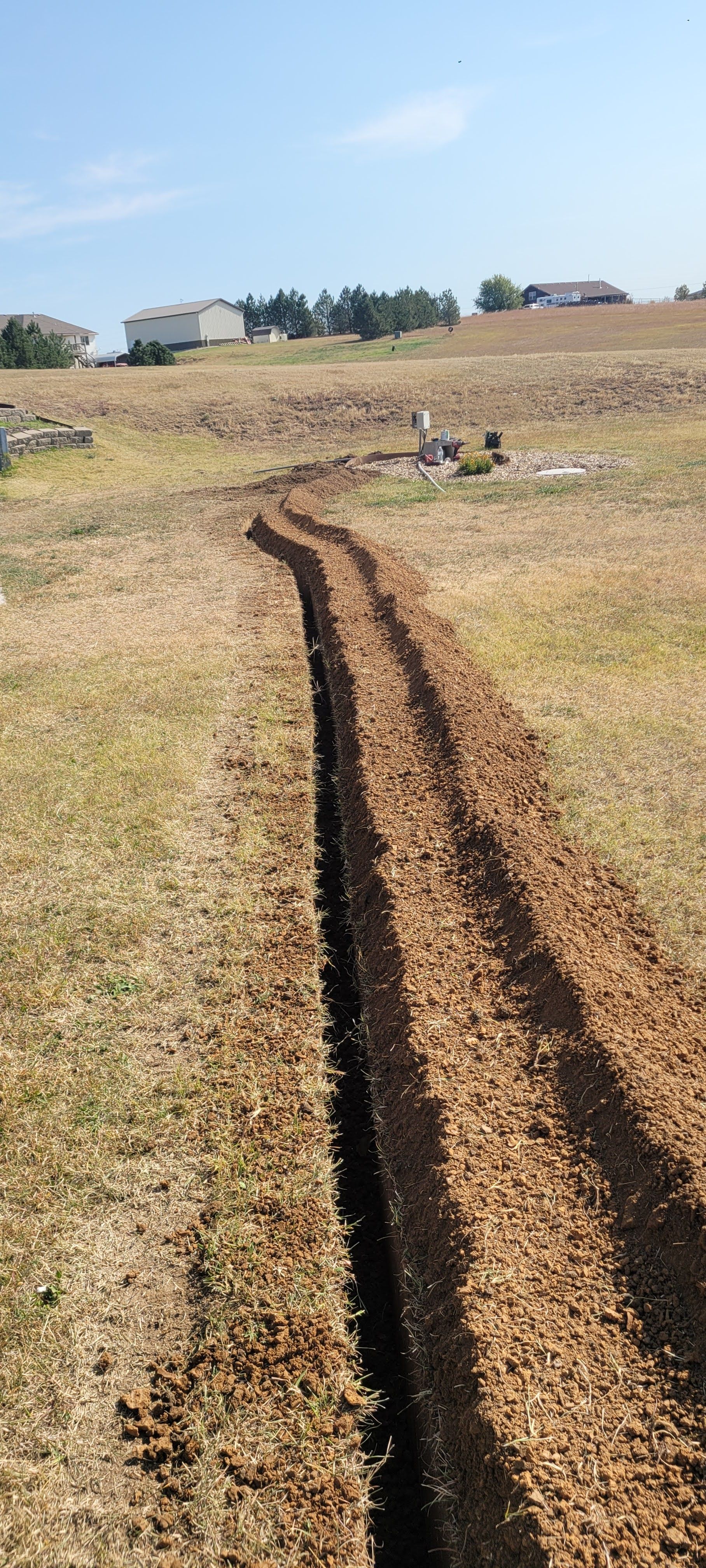 Dirt tracks cutting through a dry grassy field toward distant farm buildings under a blue sky