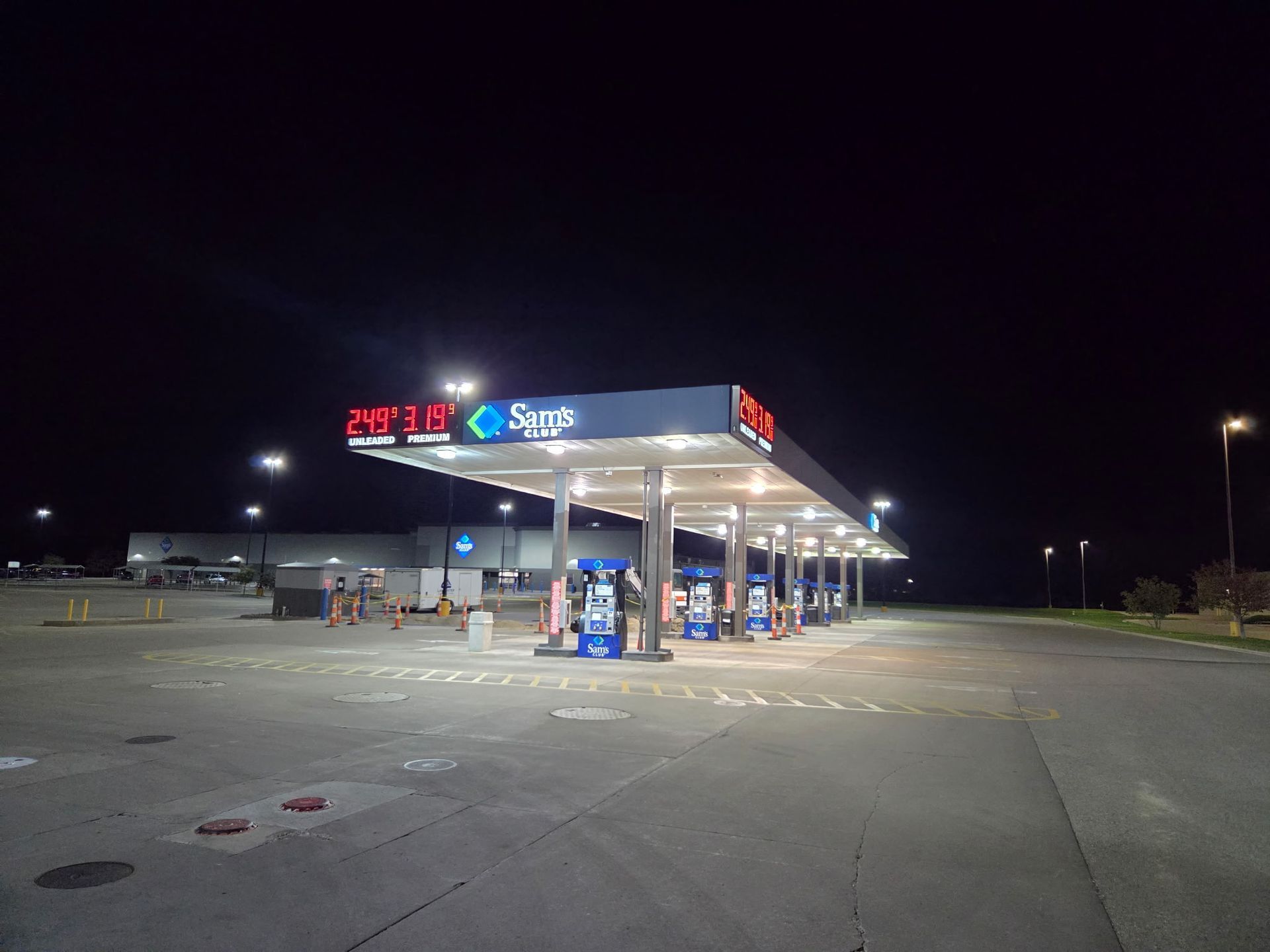 Gas station at night with bright canopy lights and a few parked vehicles across an empty lot