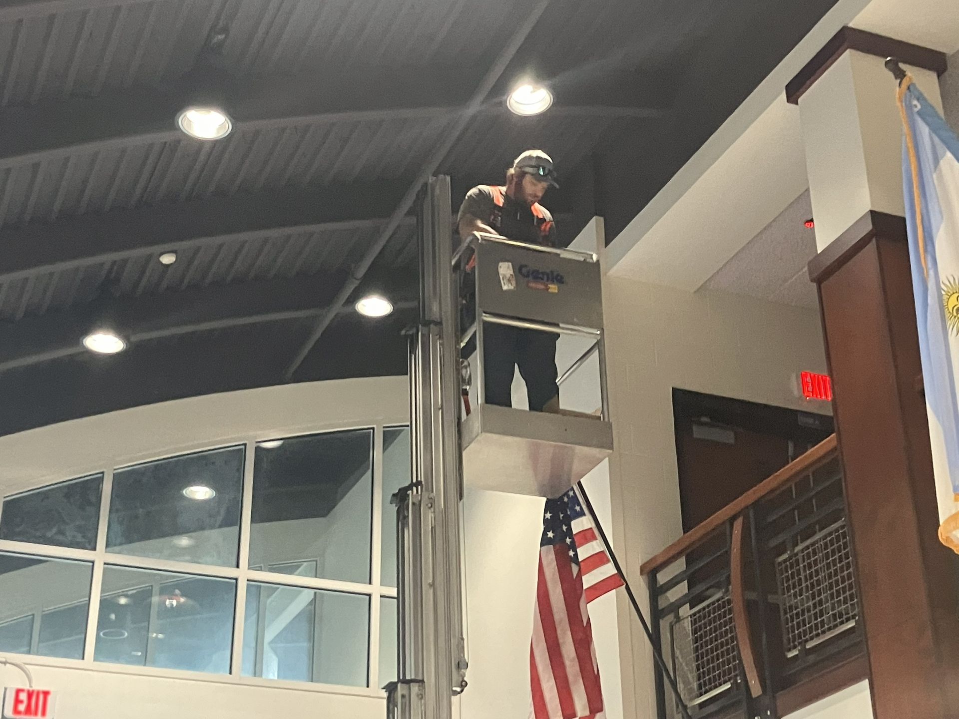 Person standing on a ladder in an indoor building near an American flag and mezzanine.