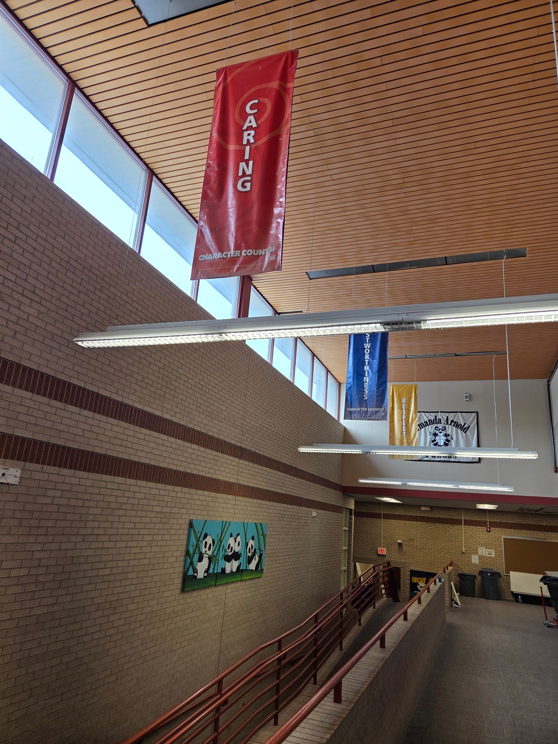 Indoor hallway with brick walls, red railings, and hanging banners under a perforated ceiling.