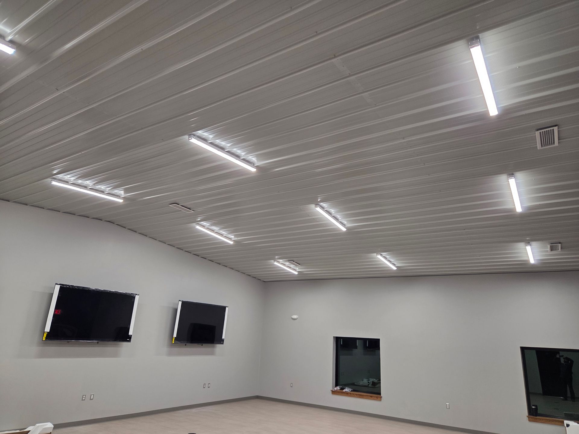 Empty room with white walls, wood floor, and several wall-mounted TVs under bright ceiling lights
