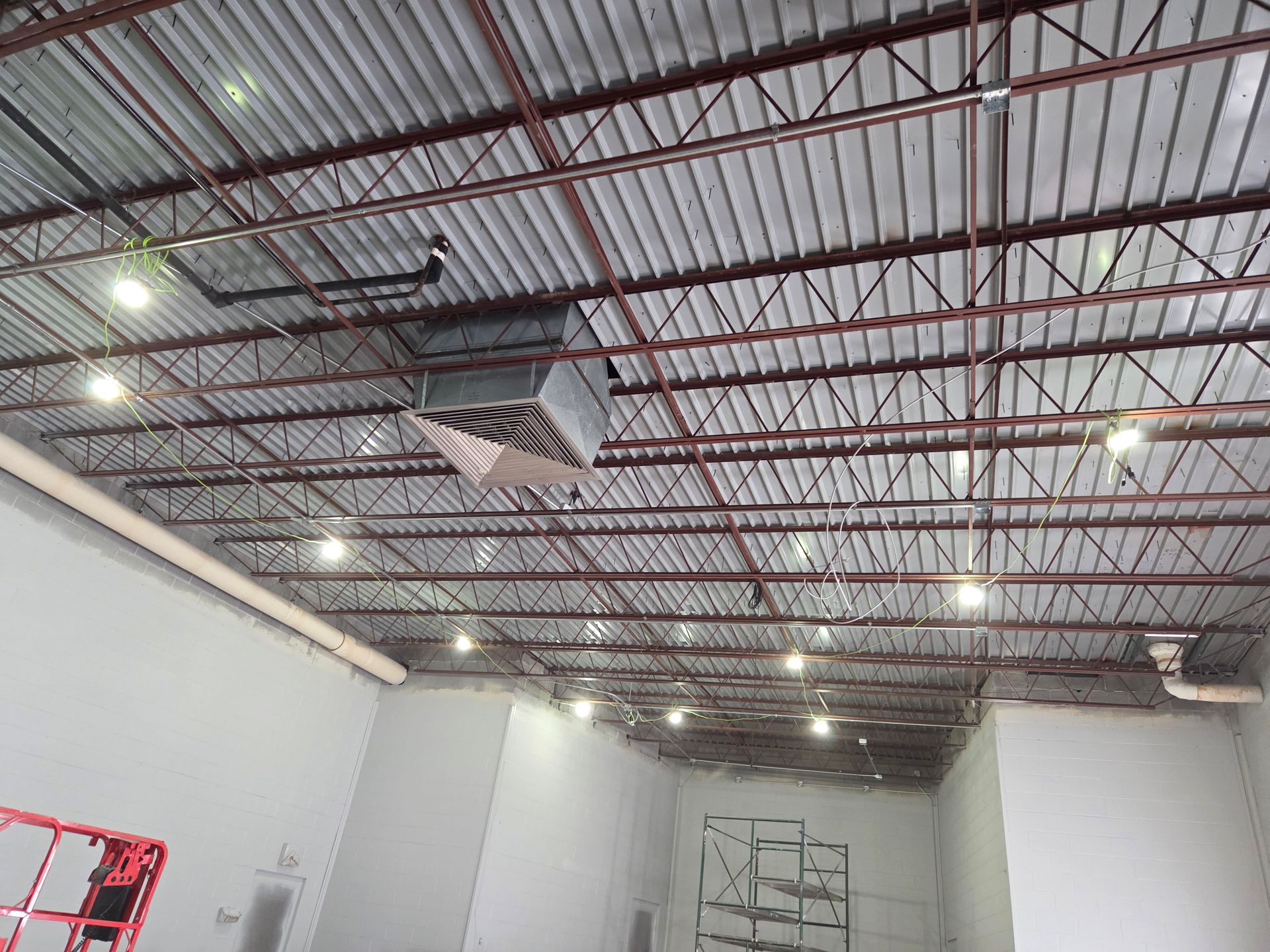 Empty industrial room with corrugated metal ceiling, exposed lights, and white walls under construction