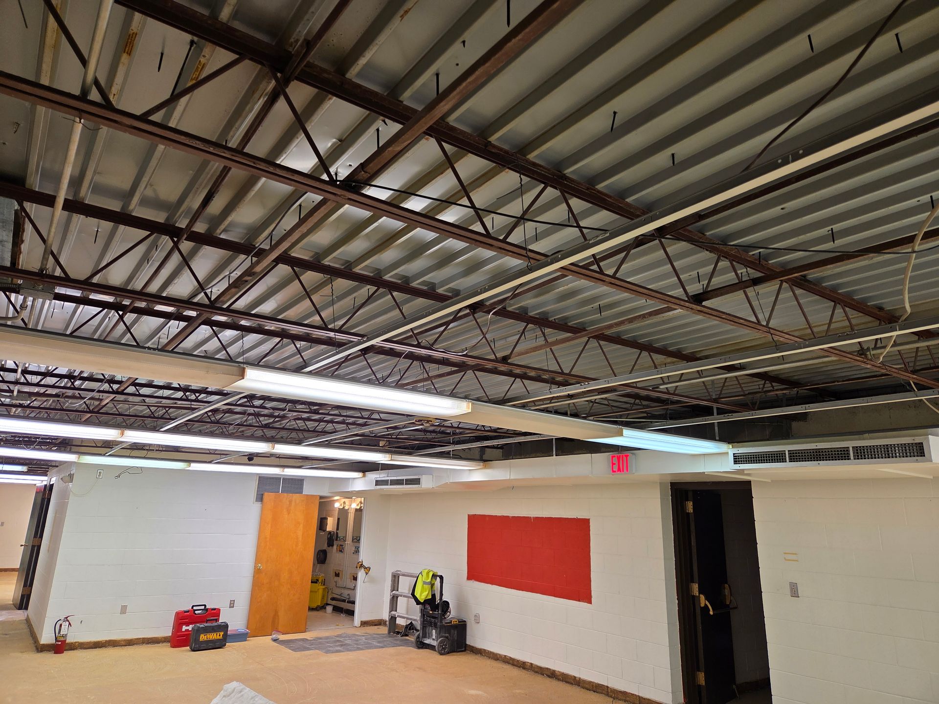 Empty warehouse interior with exposed ceiling beams, white walls, and a red panel on one wall