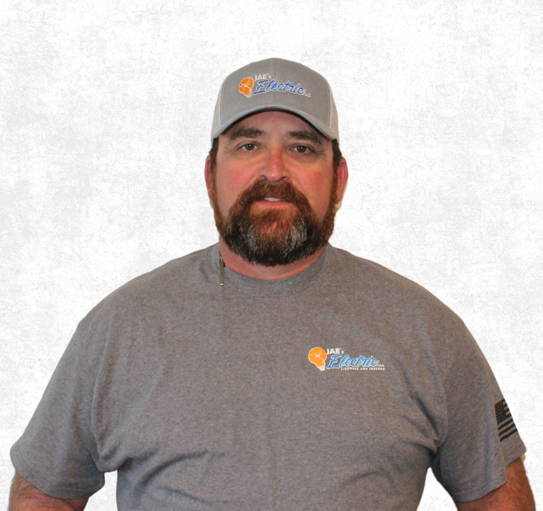 Man in gray cap and T-shirt with logo, standing against a plain light background.