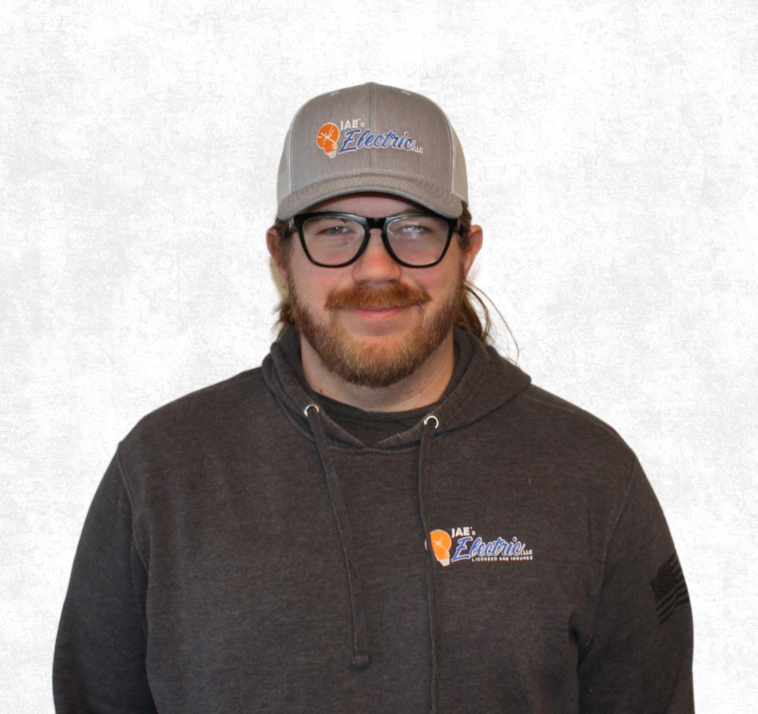 Smiling person wearing glasses, a gray cap, and dark hoodie against a plain white background