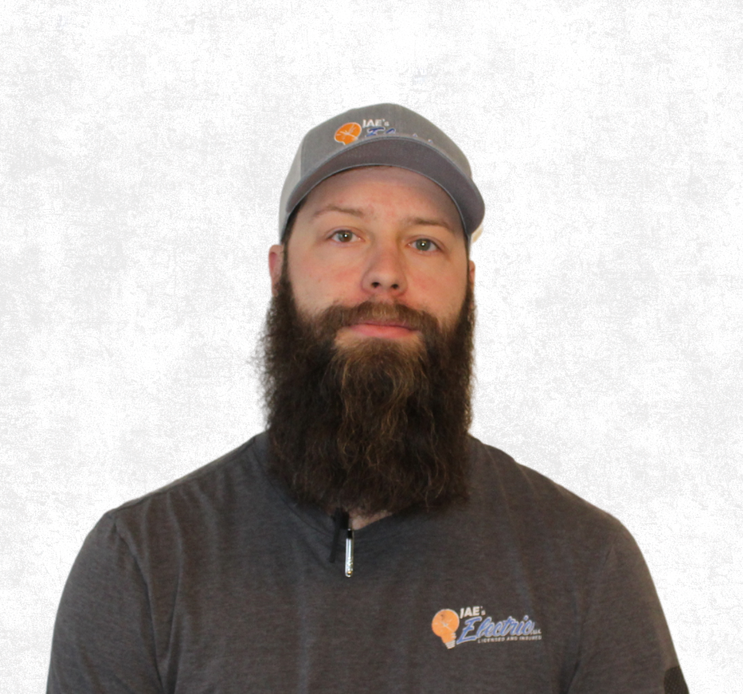 Man with a dark beard wearing a gray cap and jacket, standing against a plain light background.