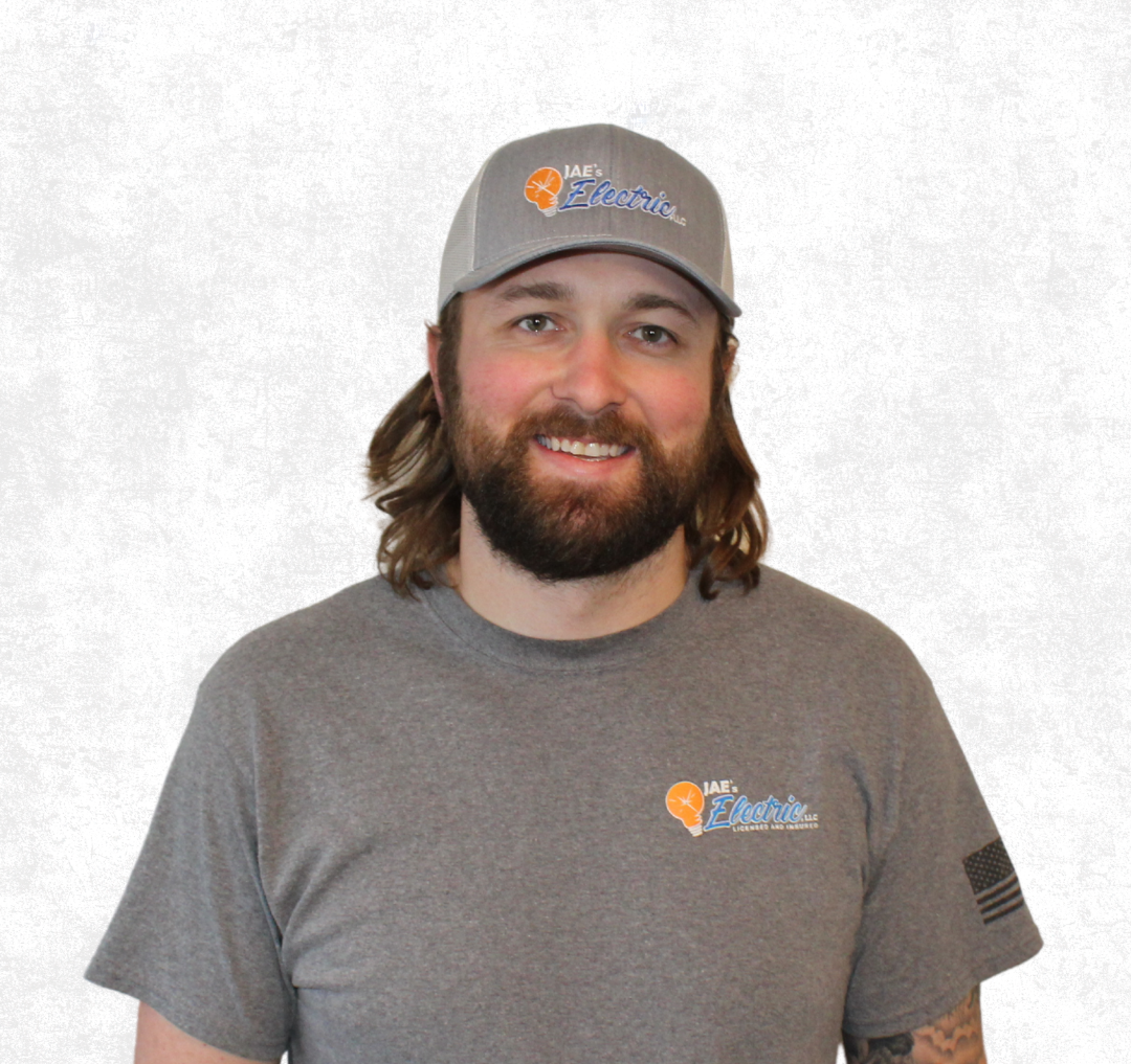 Smiling man in gray cap and shirt with logo, standing against a light background