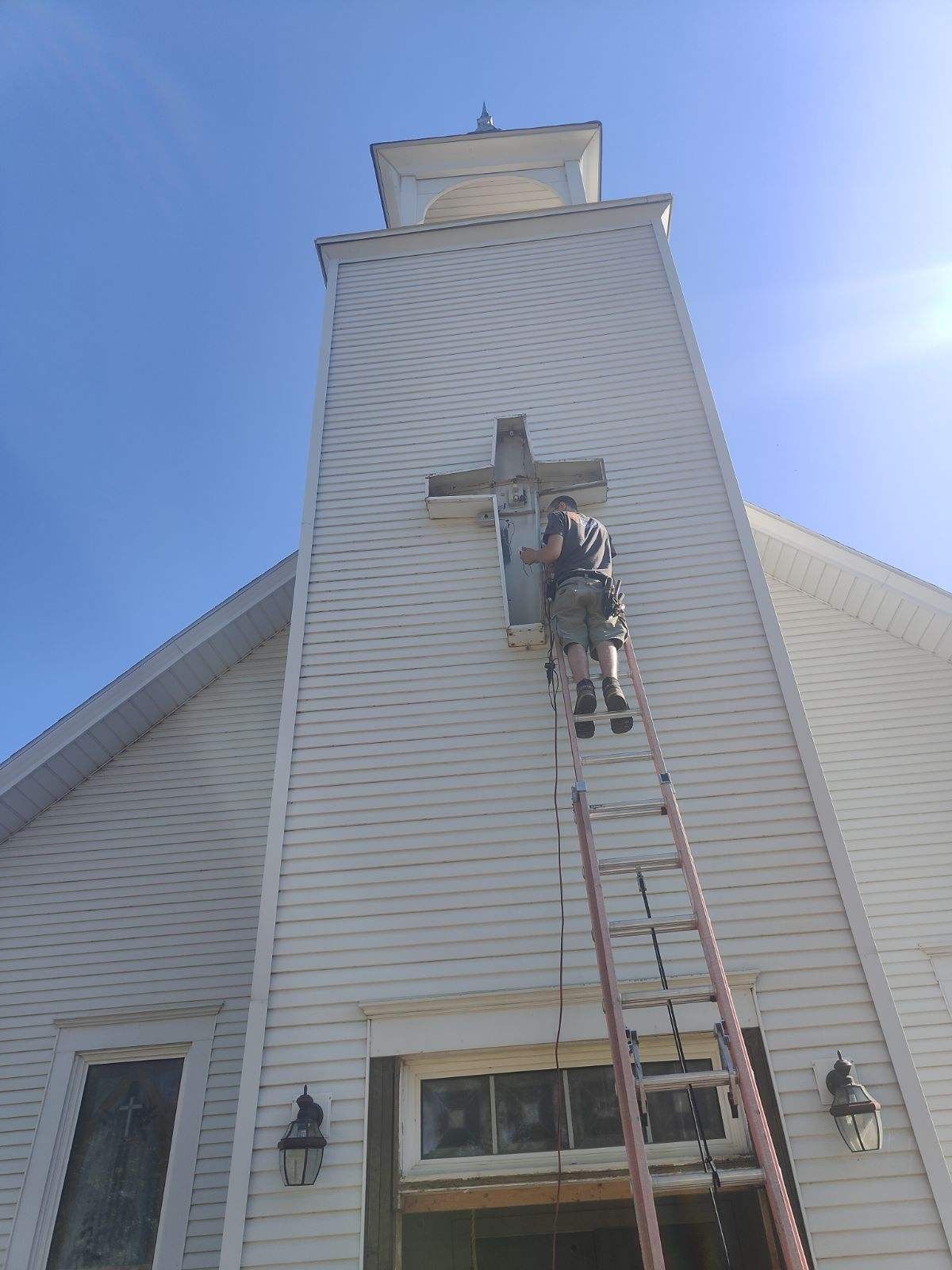 Worker on a ladder repairing a white church steeple against a blue sky