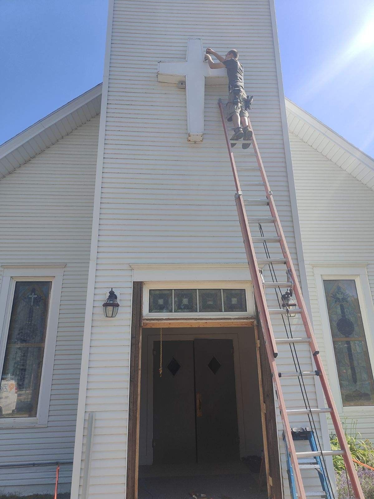 Worker on a ladder servicing a white house wall above the front entrance