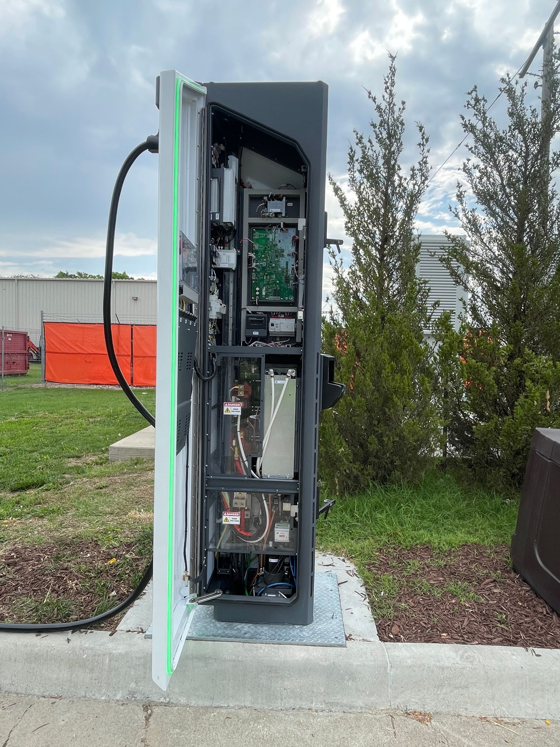 Open electrical service cabinet outdoors with exposed wiring and components beside a sidewalk.