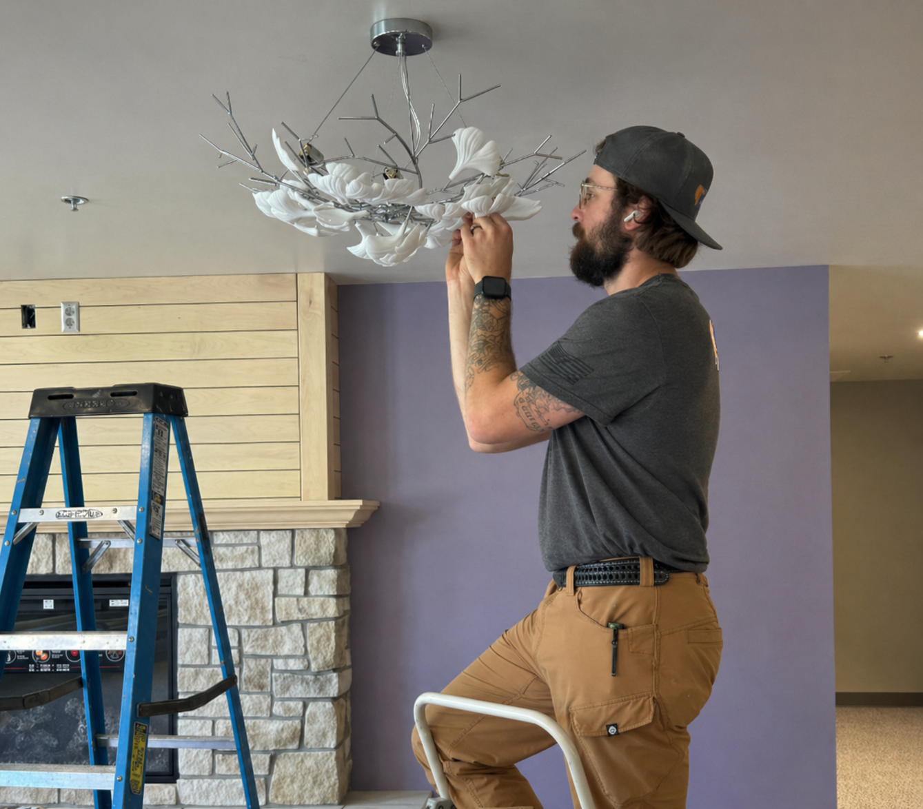 Man installing a white ceiling light fixture on a ladder in a living room under renovation