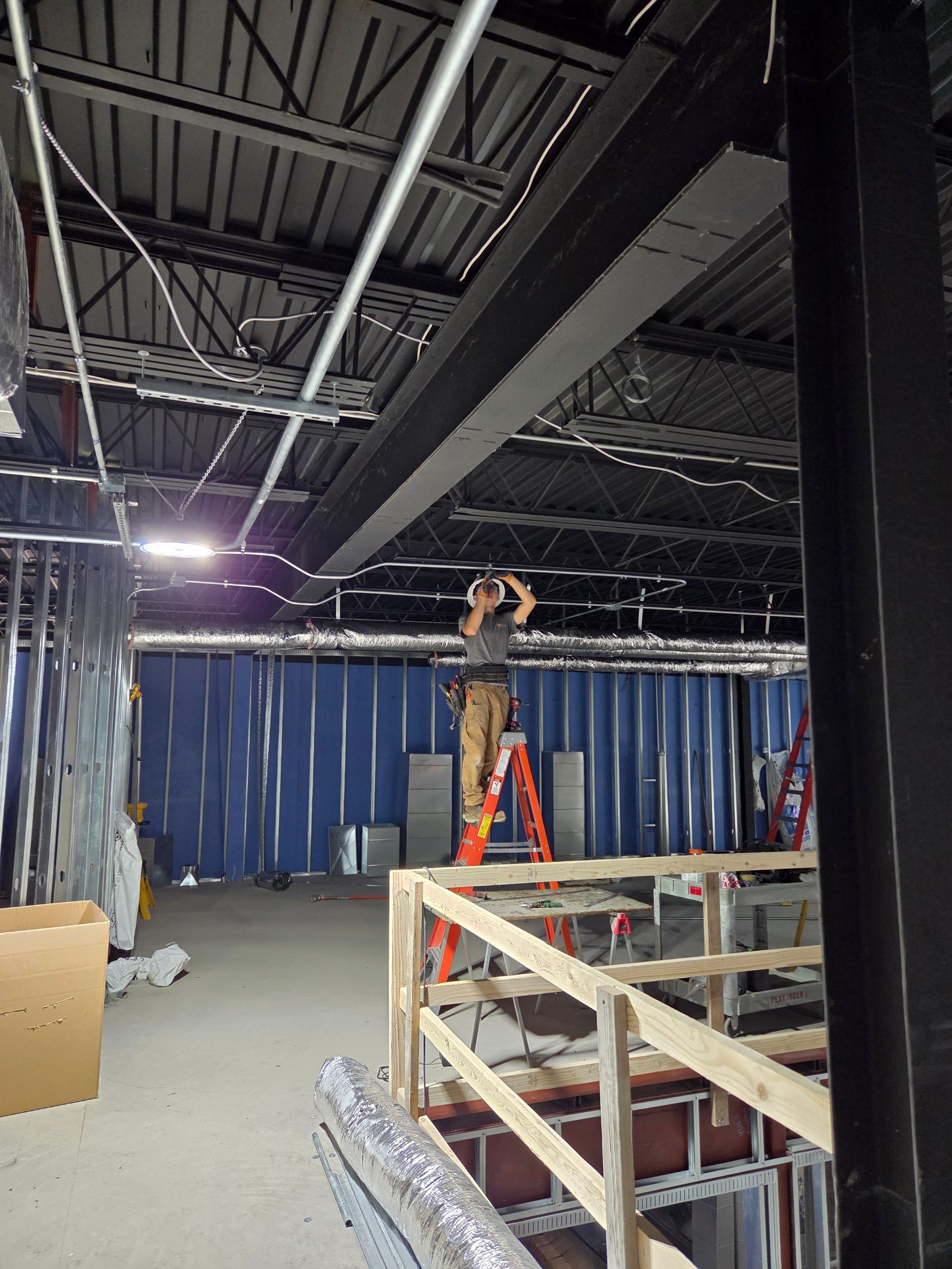 Person on a red ladder in a warehouse-like room with blue curtains and exposed ceiling beams
