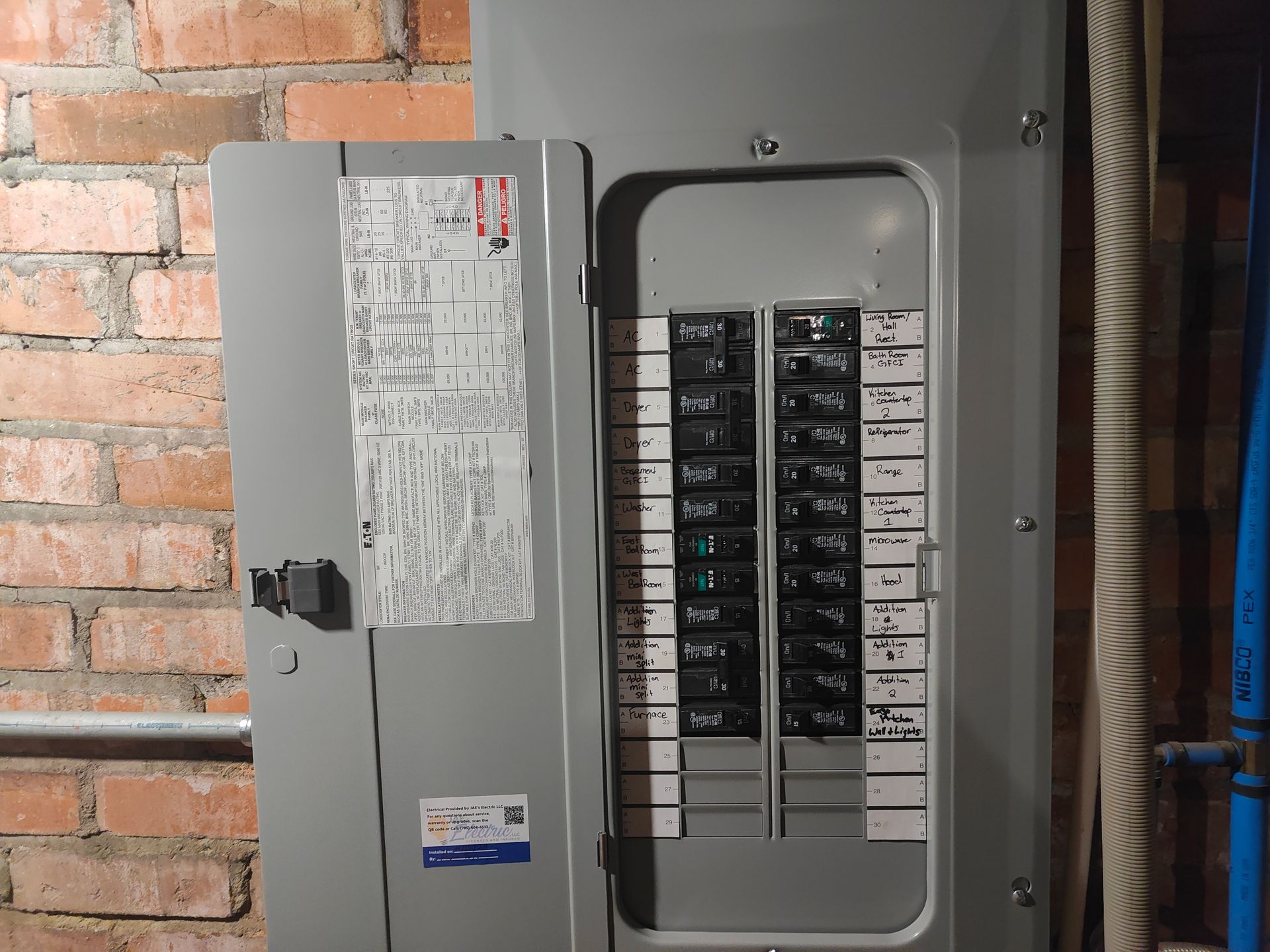 Open electrical breaker panel beside a brick wall with the cover door ajar.