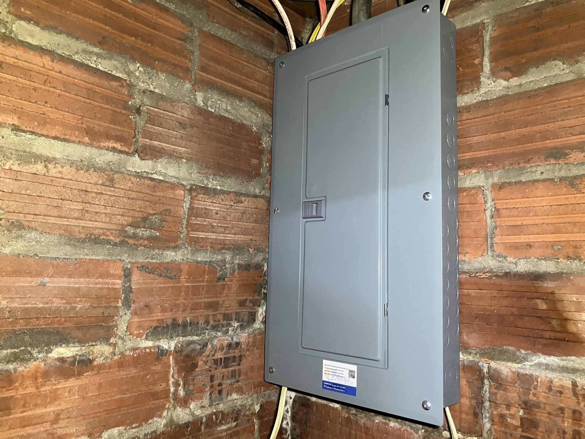 Gray electrical breaker panel mounted on a brick wall in a utility area