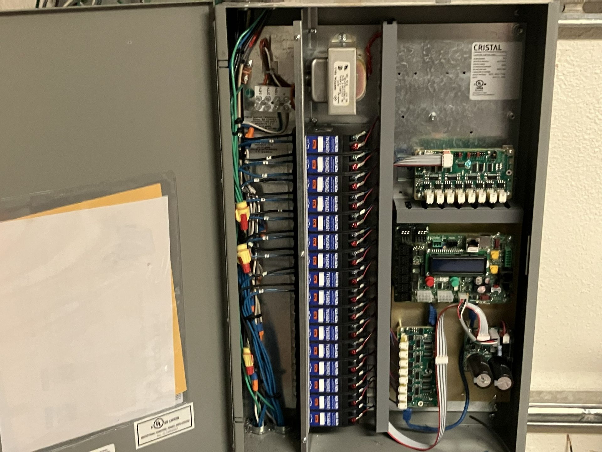 Open electrical control panel with wiring, relays, and circuit modules inside a gray cabinet.