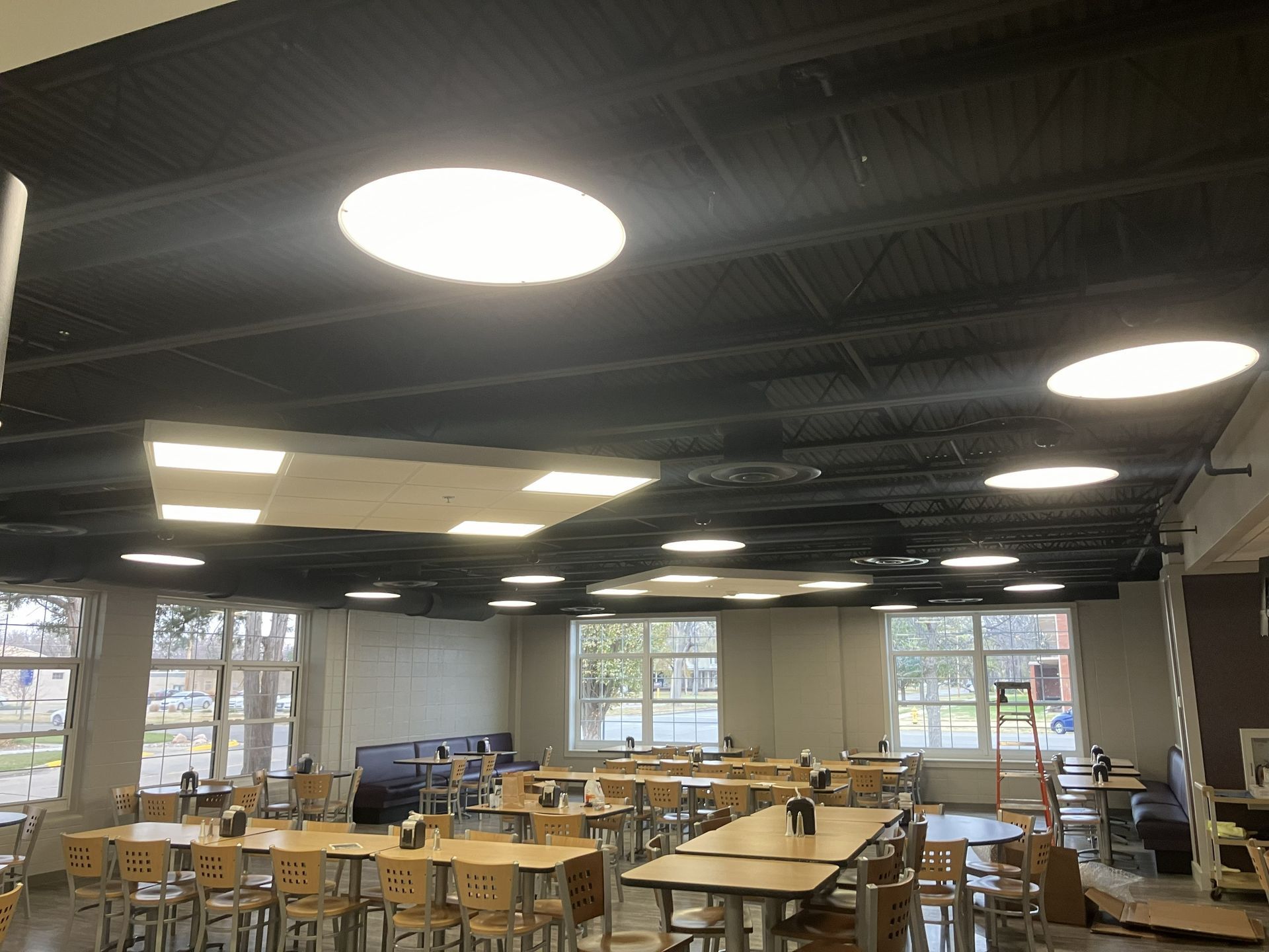 Open dining area with wooden tables and chairs under bright circular ceiling lights.