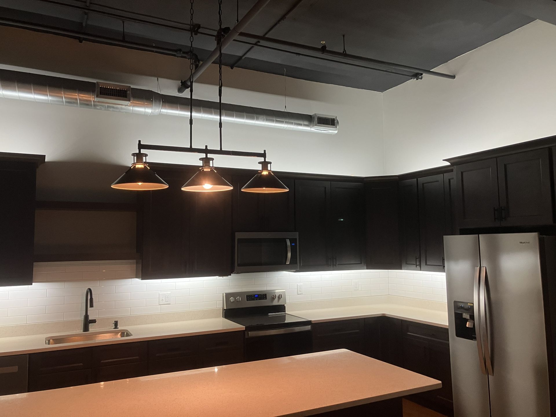 Modern kitchen with dark cabinets, stainless steel fridge, pendant lights, and a white island countertop