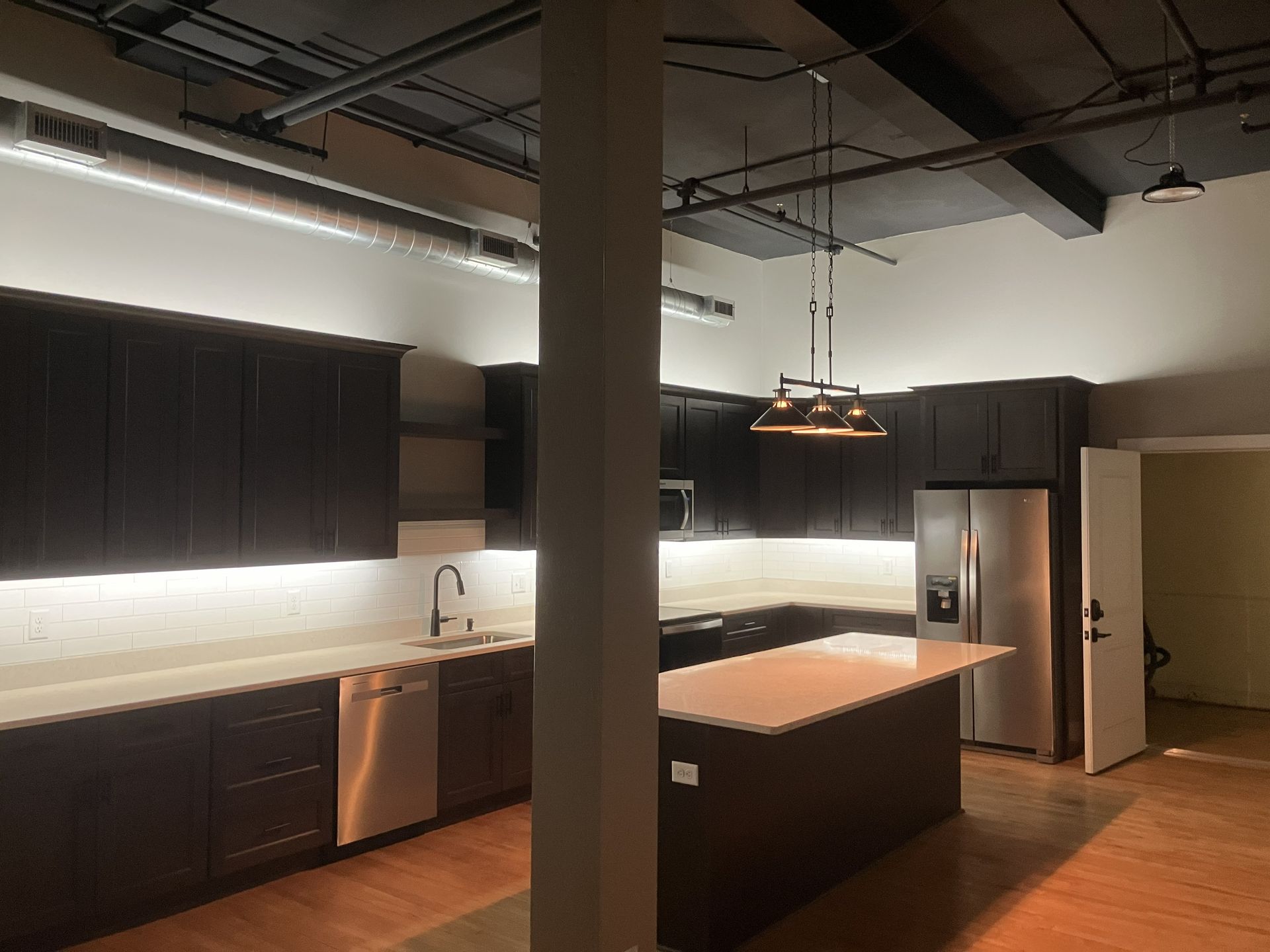Modern kitchen with dark cabinets, central island, stainless fridge, and pendant lights