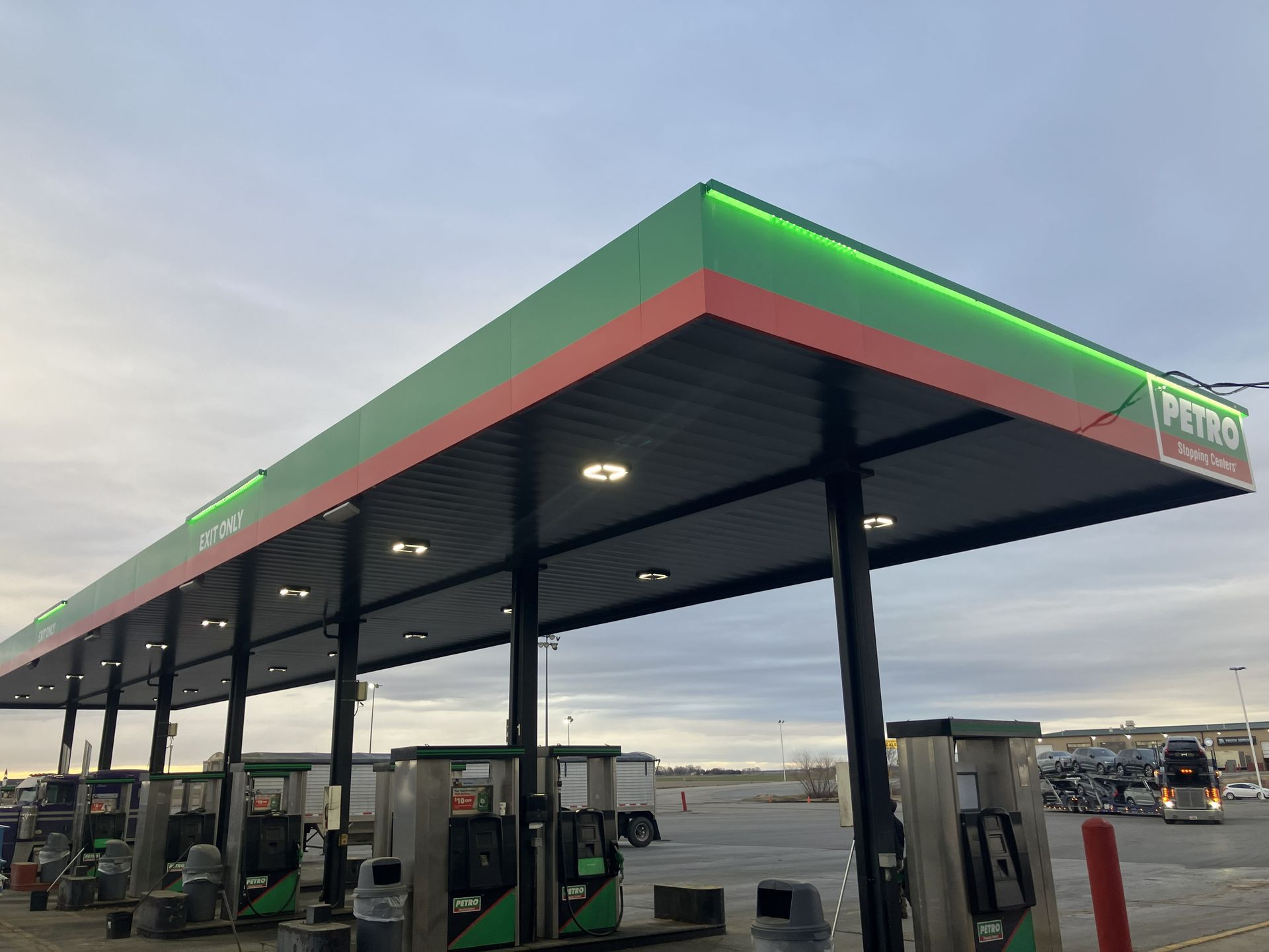 Gas station canopy at dusk with green-lit trim and fuel pumps underneath