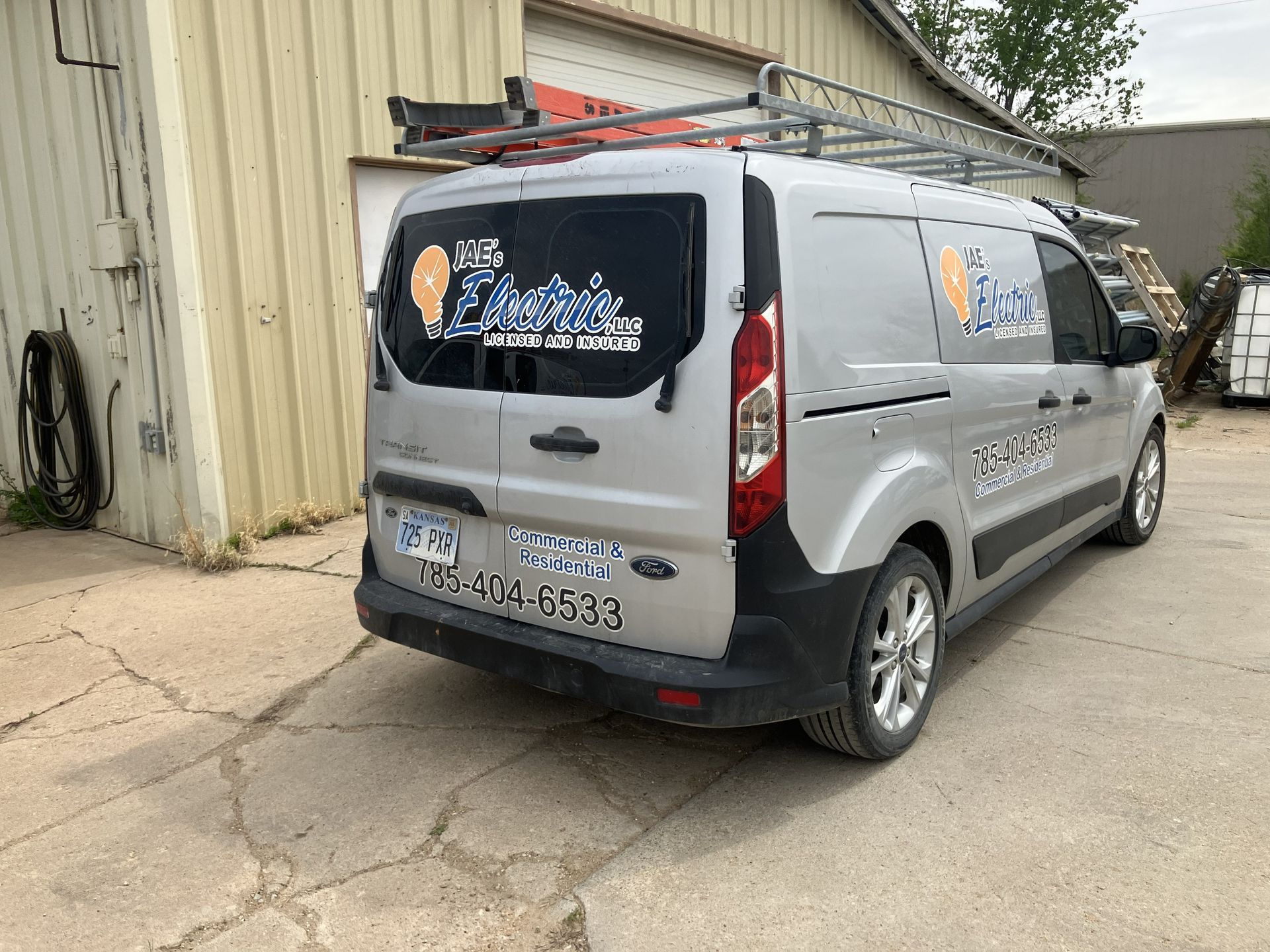 Gray commercial van parked beside a beige building, rear view with decals on the back window.