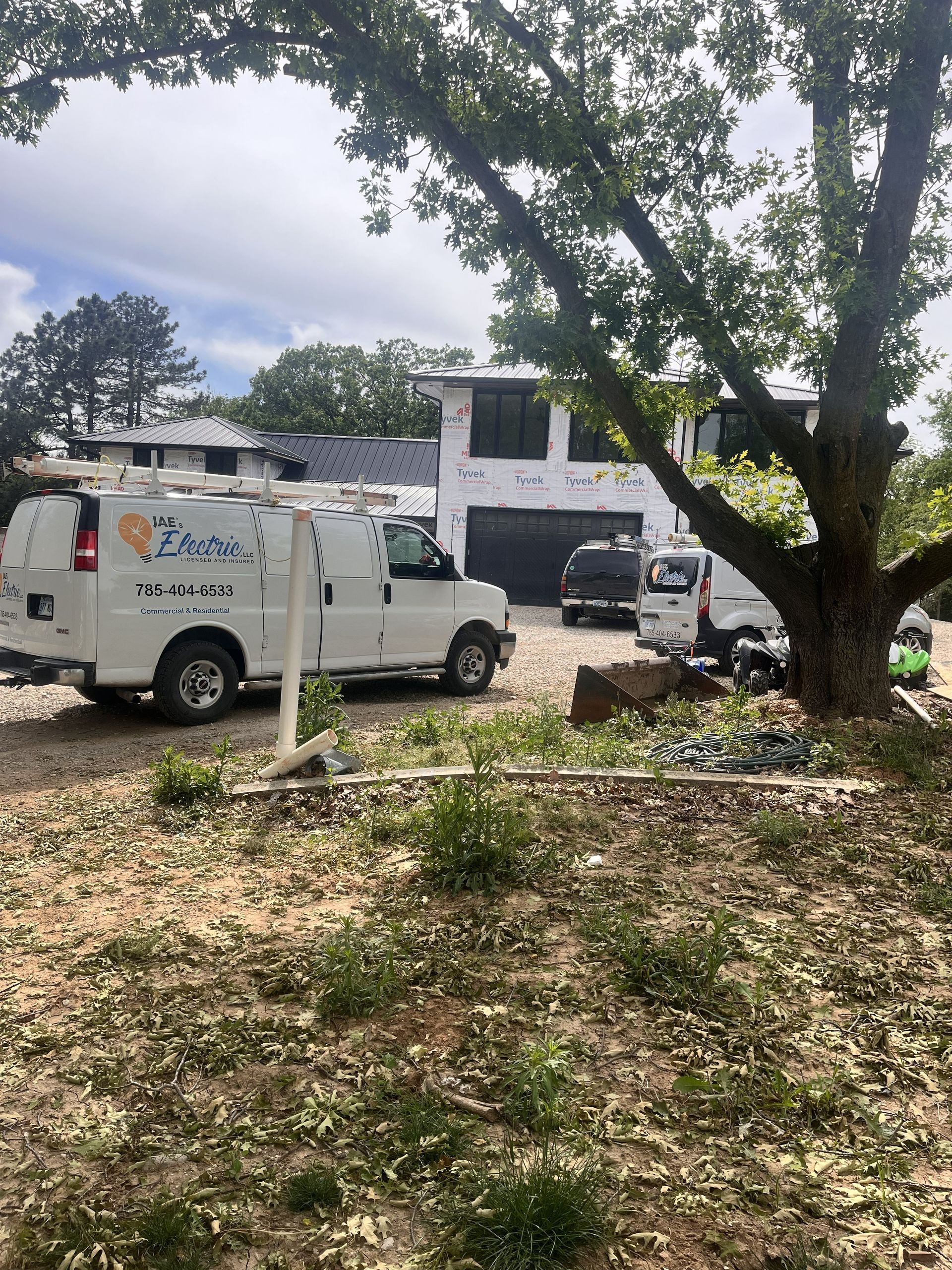 White utility van parked by a house under a large tree with another dark vehicle nearby