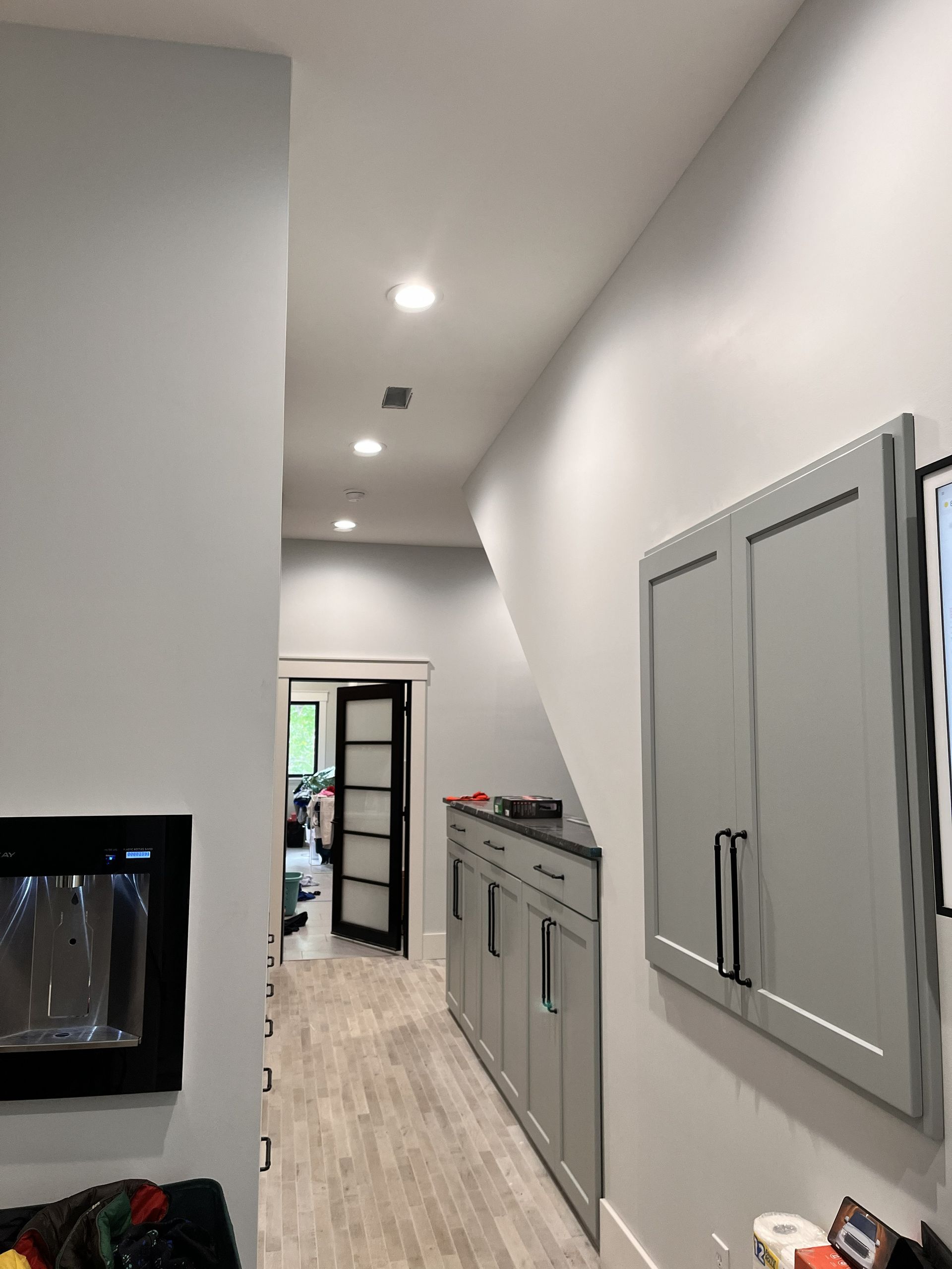 Narrow modern hallway with gray cabinets, recessed lights, and a fireplace on the left.