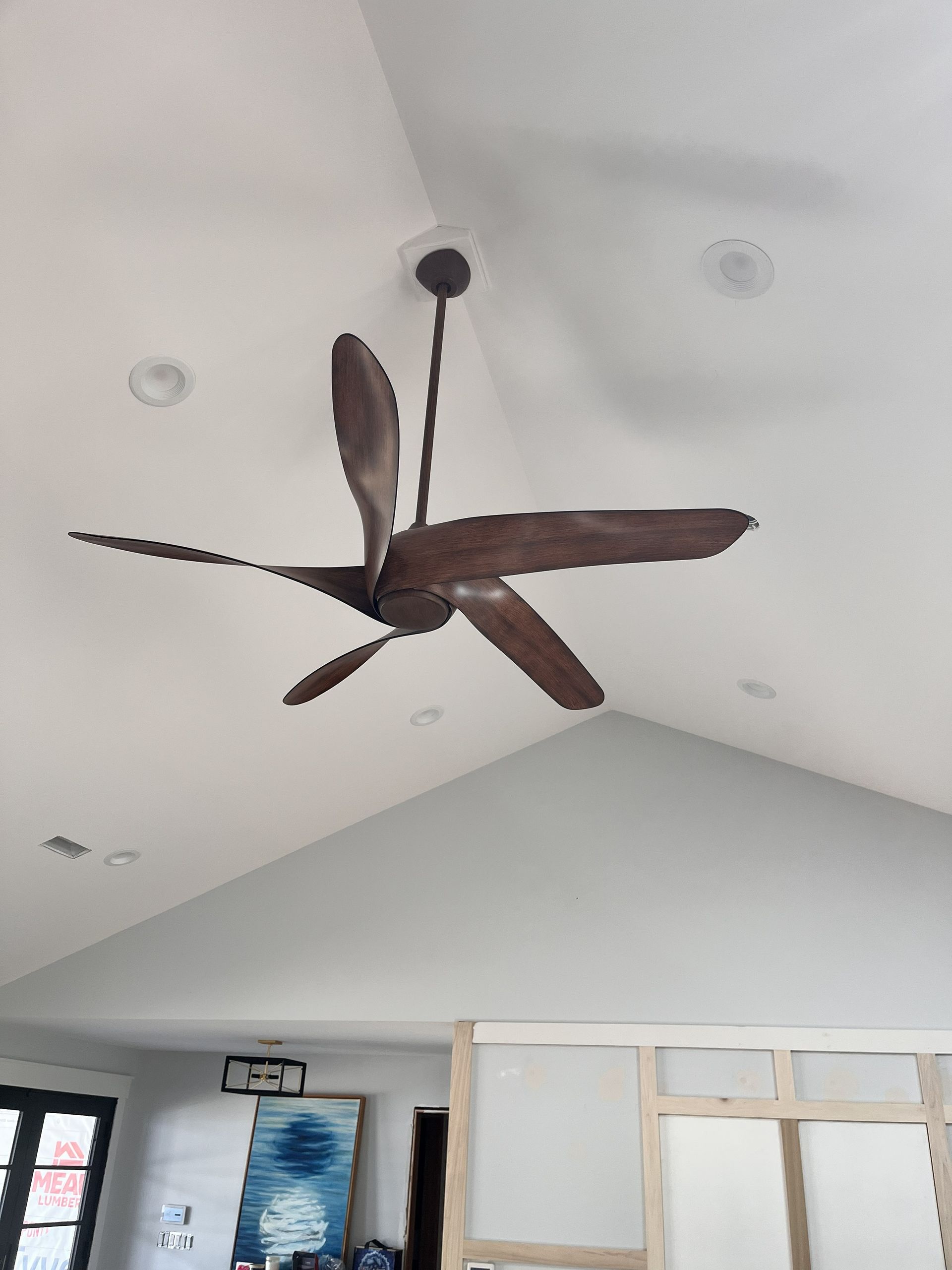 Modern ceiling fan with wood blades hanging from a white vaulted ceiling in a bright room