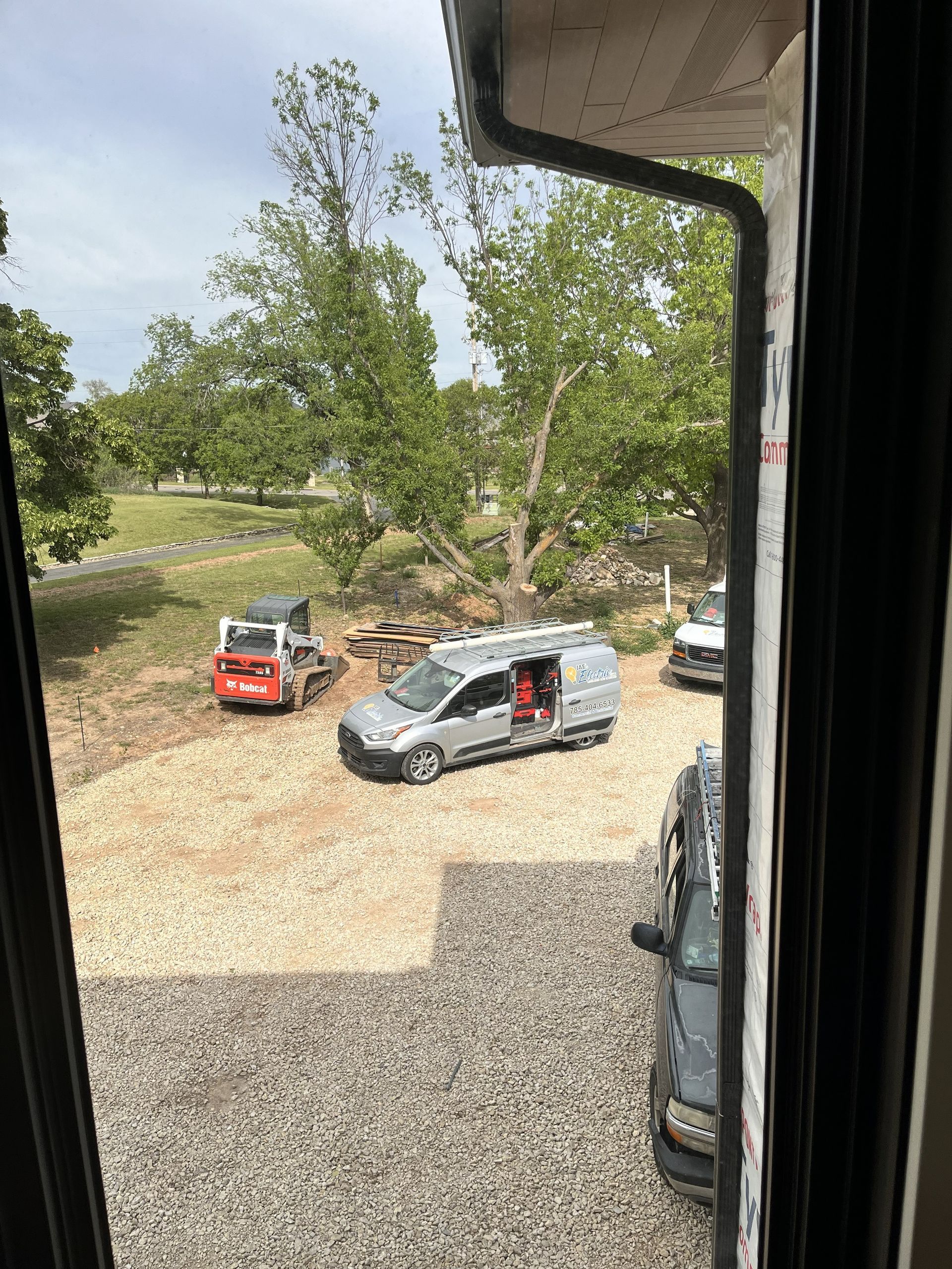 Red and silver cars parked on a gravel driveway beside trees, viewed from a window