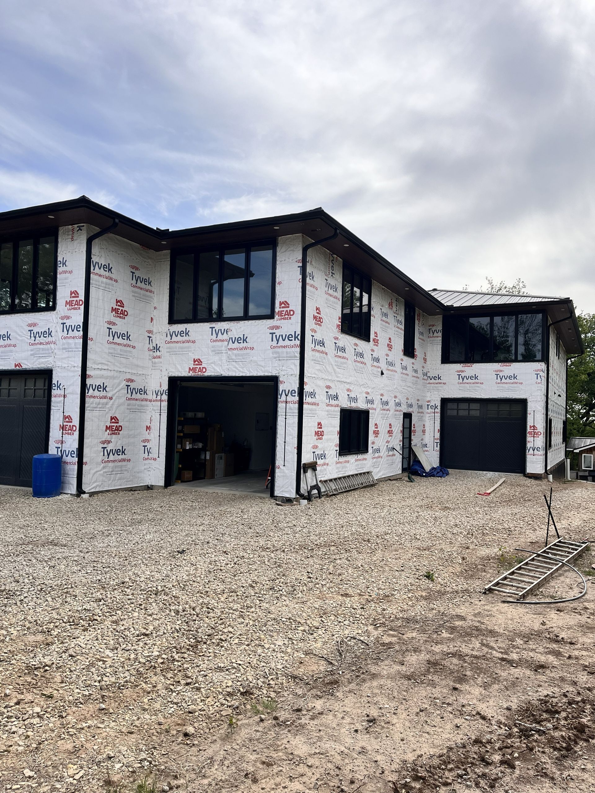 Two-story house under construction, wrapped in white insulation with black trim and gravel foreground