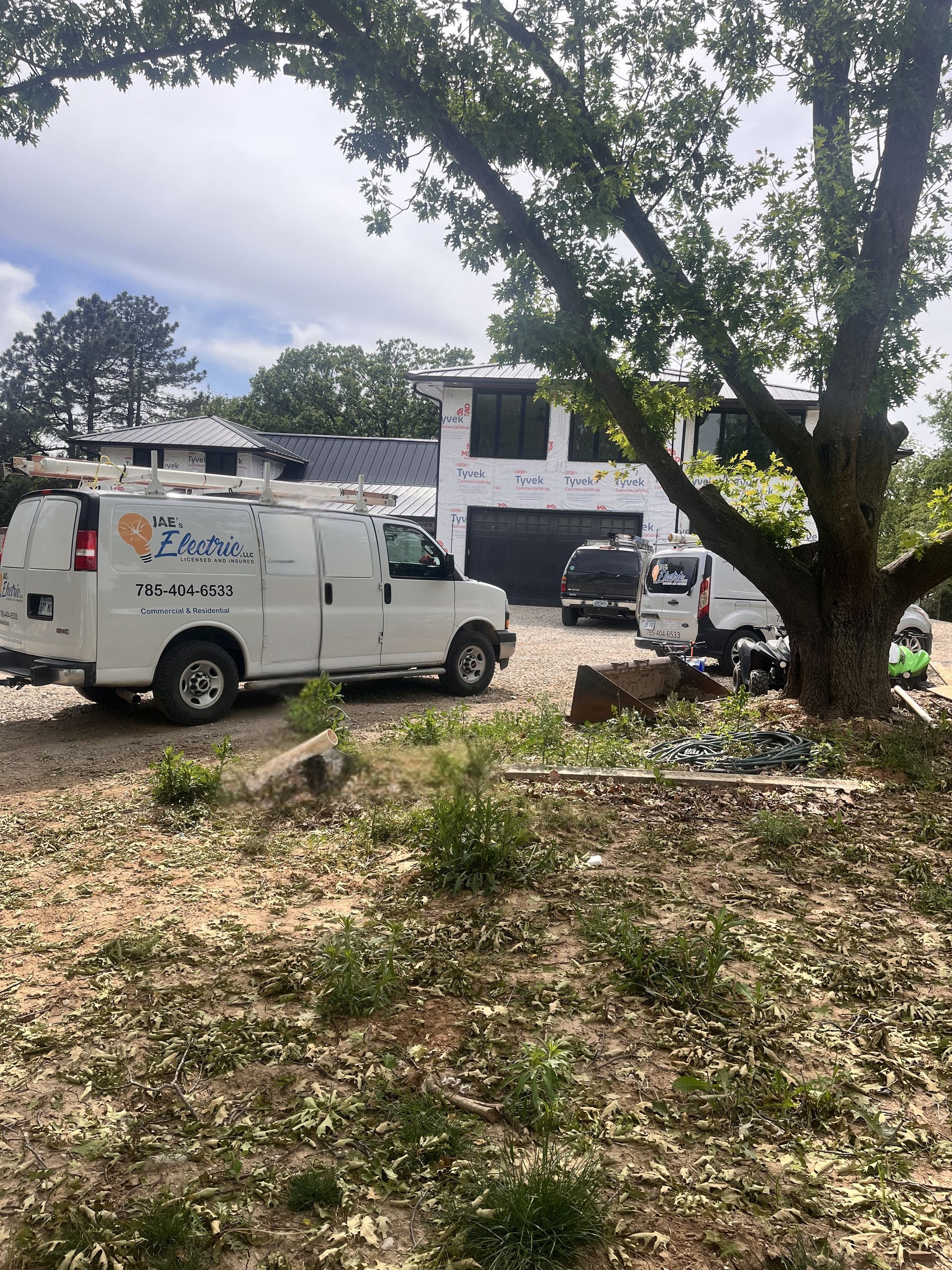 White utility van and black SUV parked near a house under a tree on a leaf-covered yard.