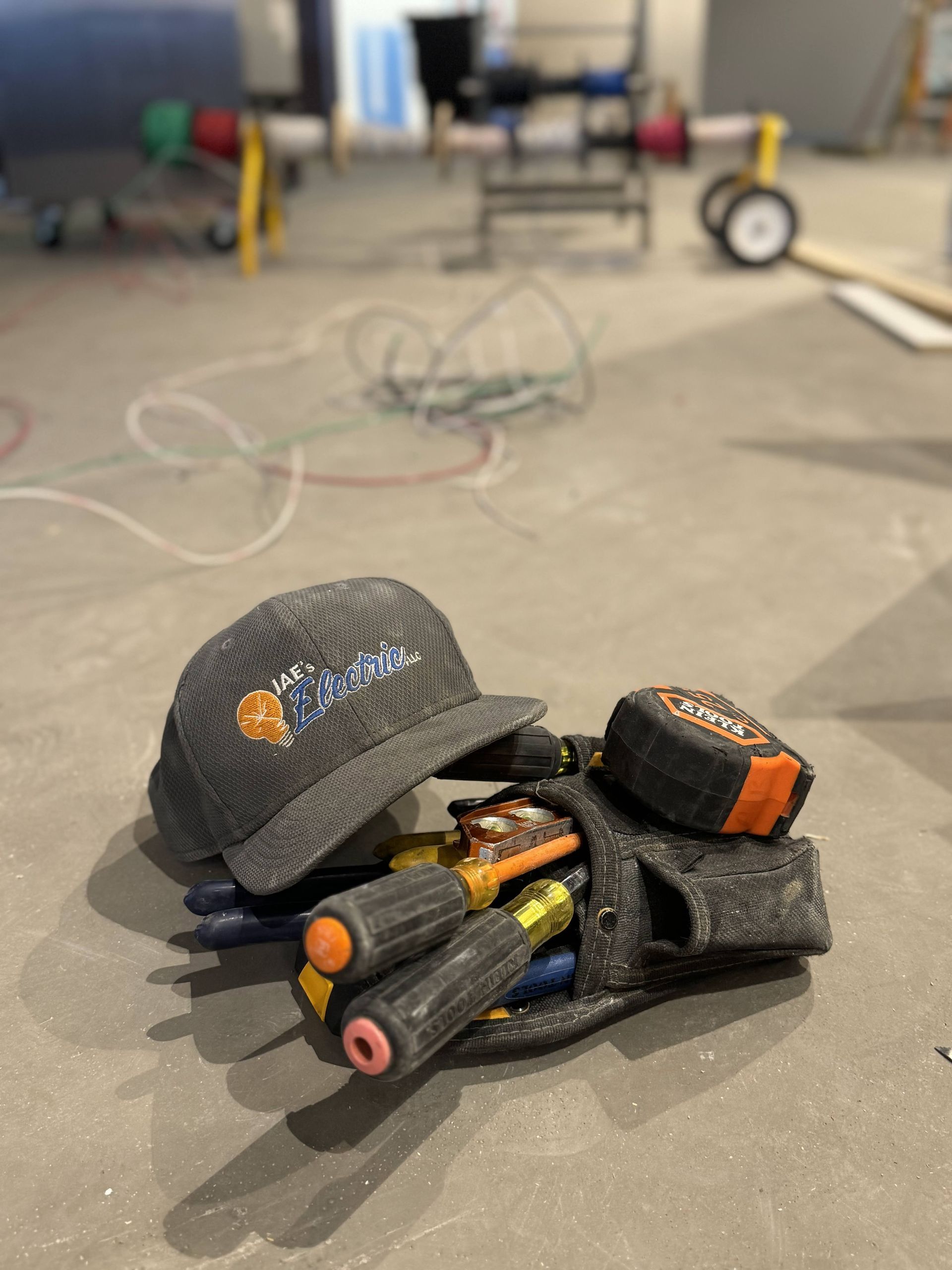 Black cap and several orange-tipped batteries on a concrete floor, with workshop equipment blurred in the background