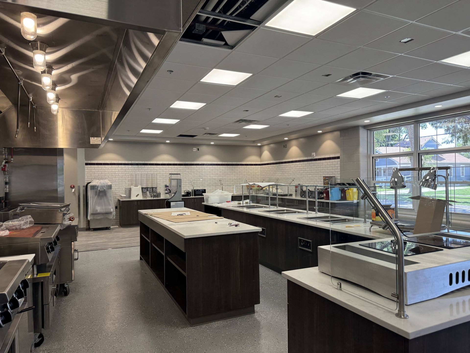 Empty commercial kitchen with stainless steel counters, prep islands, and bright overhead lighting.
