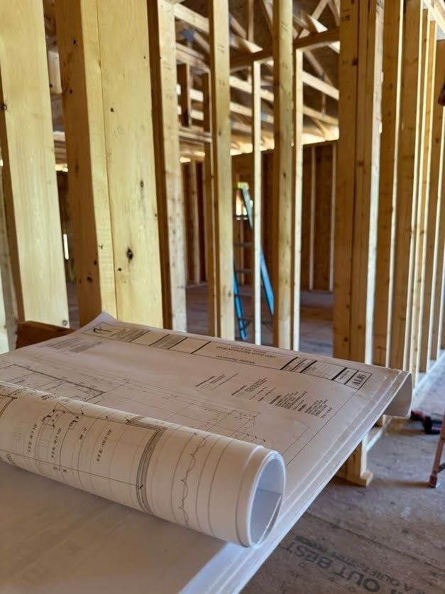 Construction plans on a table inside a framed house under construction.