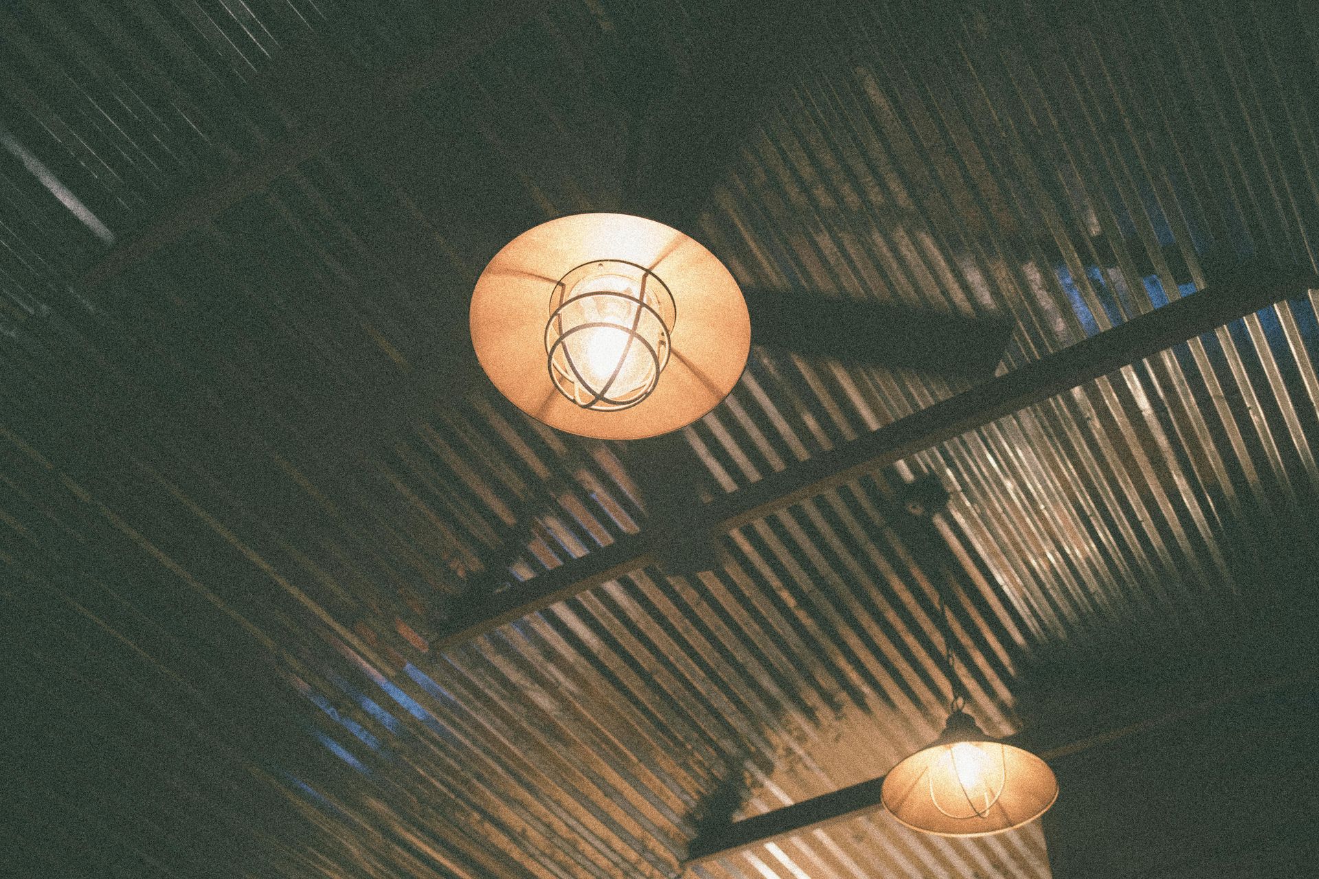 Two warm pendant lights hanging from a dark, corrugated ceiling with diagonal shadows
