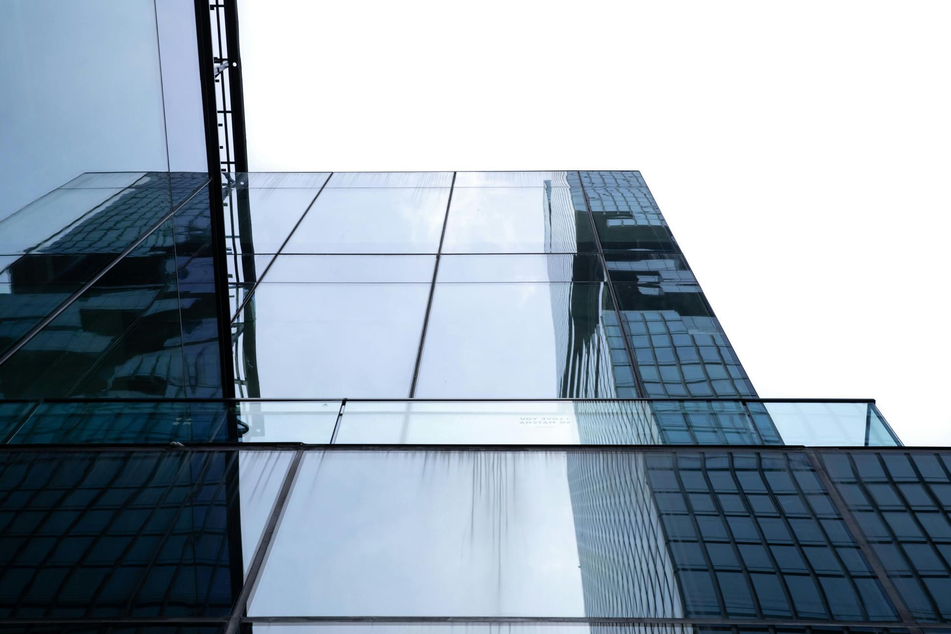 Modern glass office building facade reflecting the sky and neighboring tower
