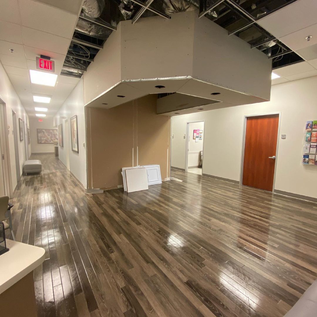 A long hallway with wooden floors and a red exit sign on the ceiling.