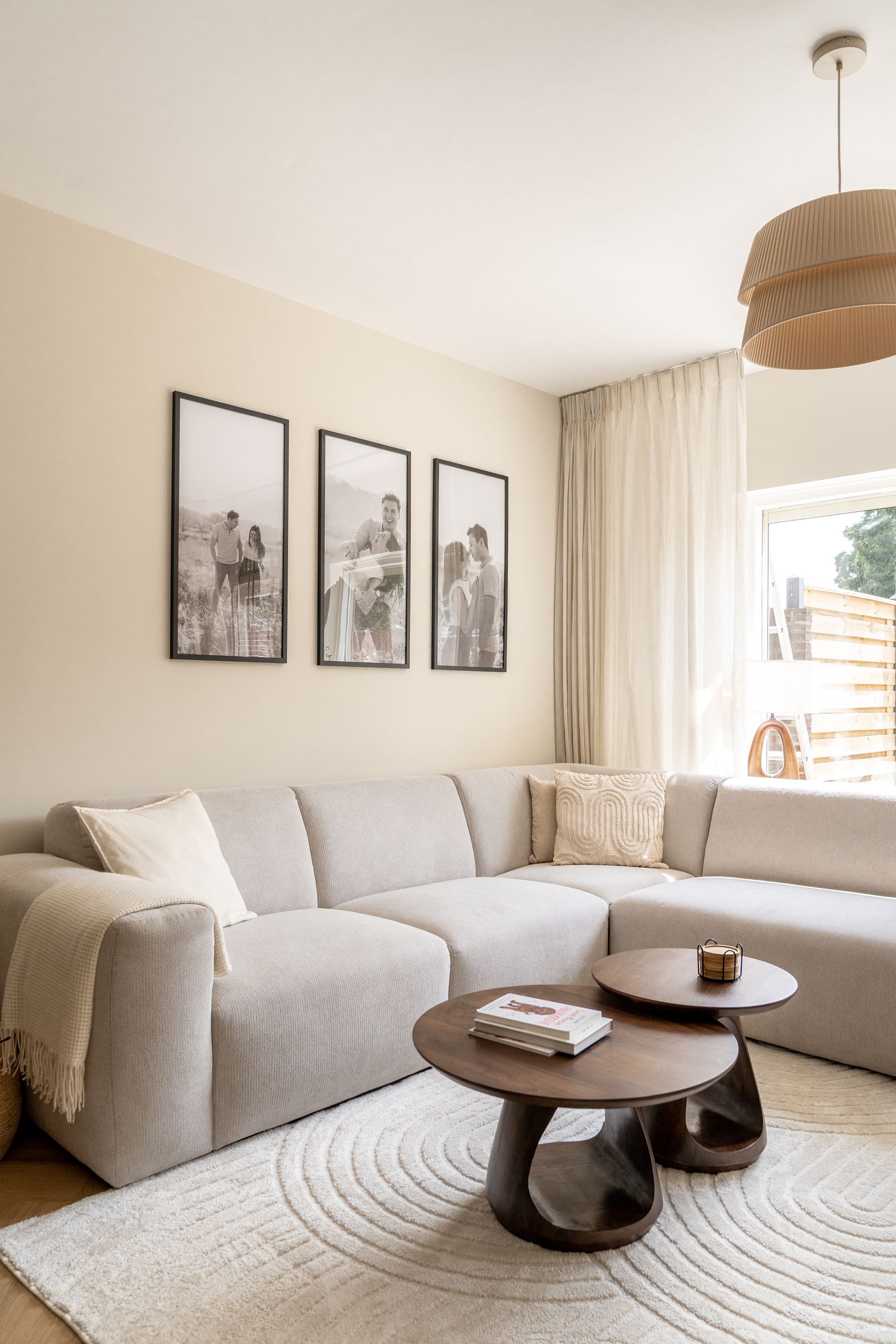 Een woonkamer in neutrale tinten met een grote lichtgrijze hoekbank, twee ronde houten salontafels en wanddecoratie.
