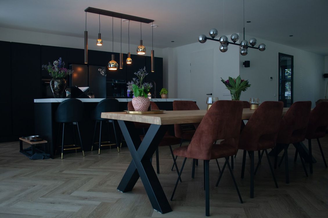 Een moderne keuken en eethoek met een houten tafel, bruine stoelen, zwarte krukken en design hanglampen.