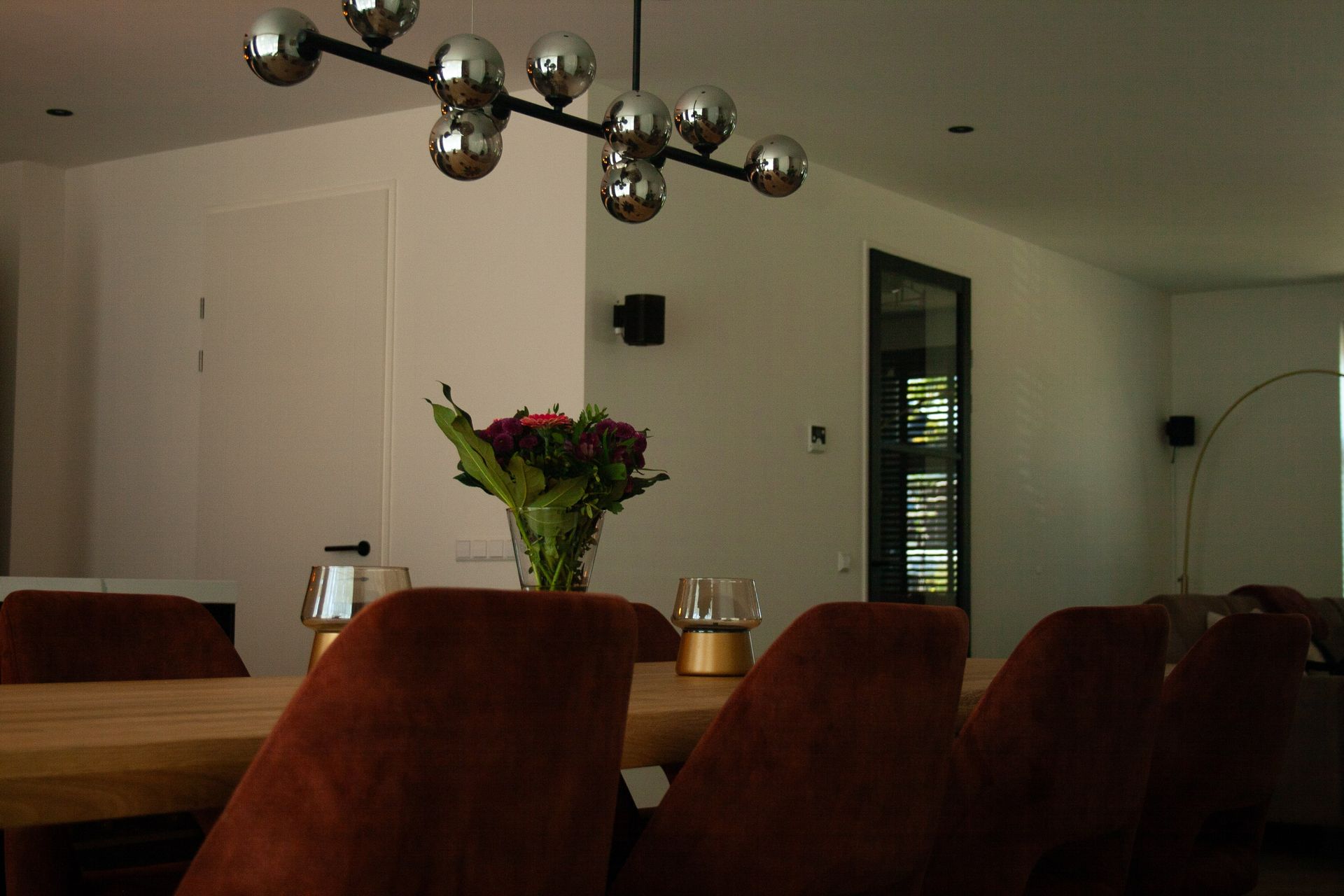 Een eetkamer met een houten tafel, rode stoelen en een moderne kroonluchter met meerdere lampen erboven.