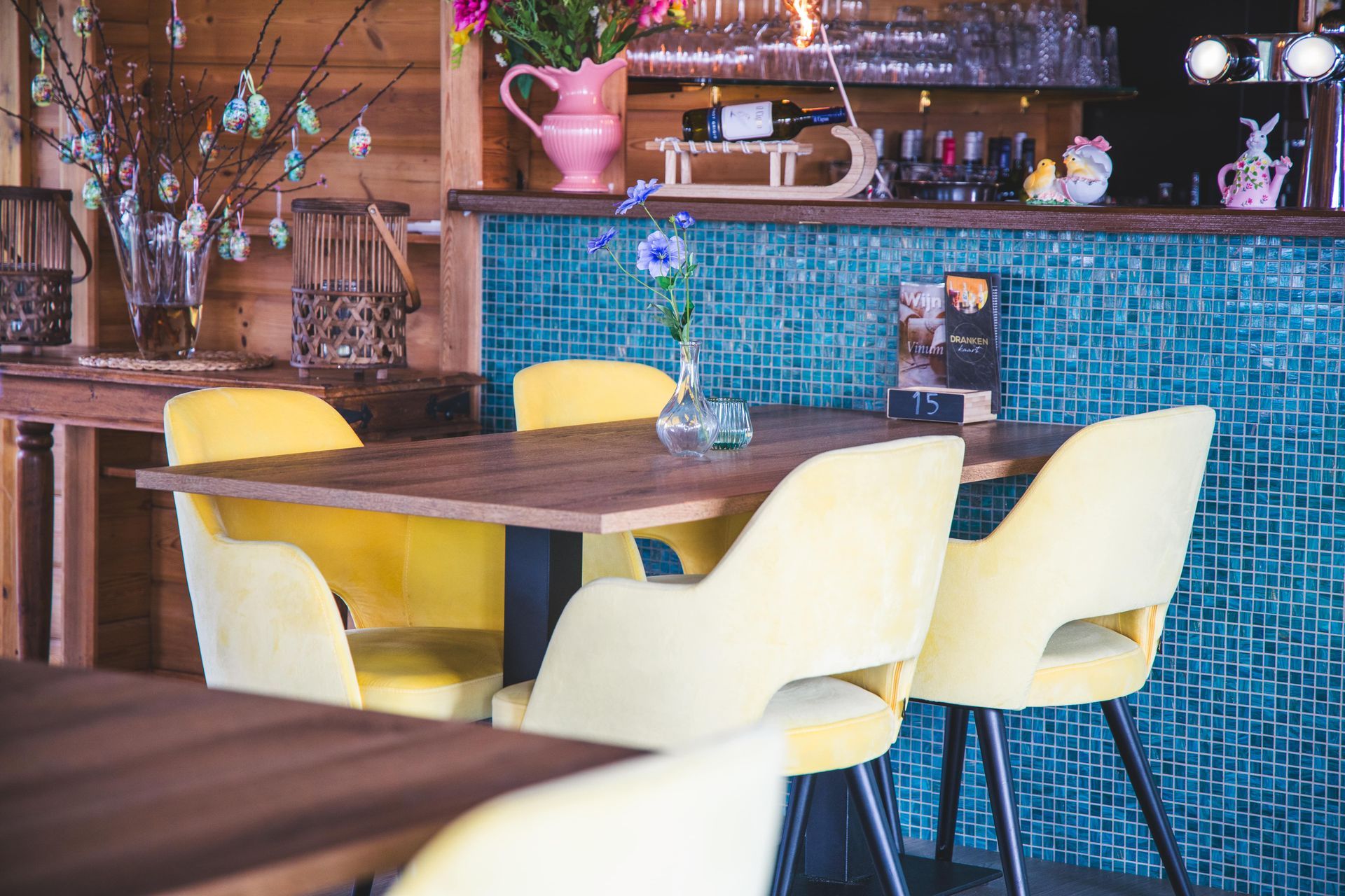 Een digitale interieurweergave van een restaurant met blauwe en gele stoelen, wit servies en hangende bolvormige lampen.