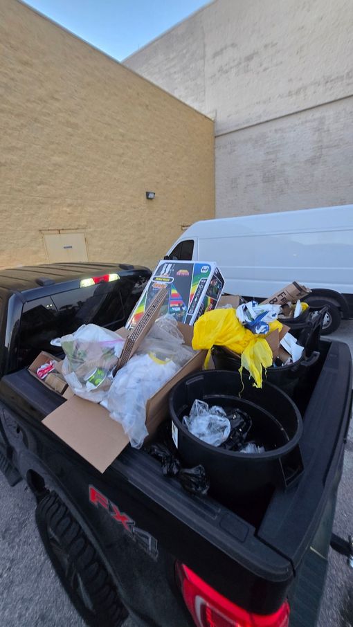 Overflowing black trash bin with mixed garbage beside a beige wall outdoors