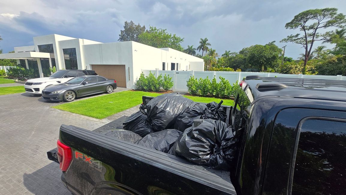 Black pickup truck bed loaded with trash bags outside a white building on a sunny day