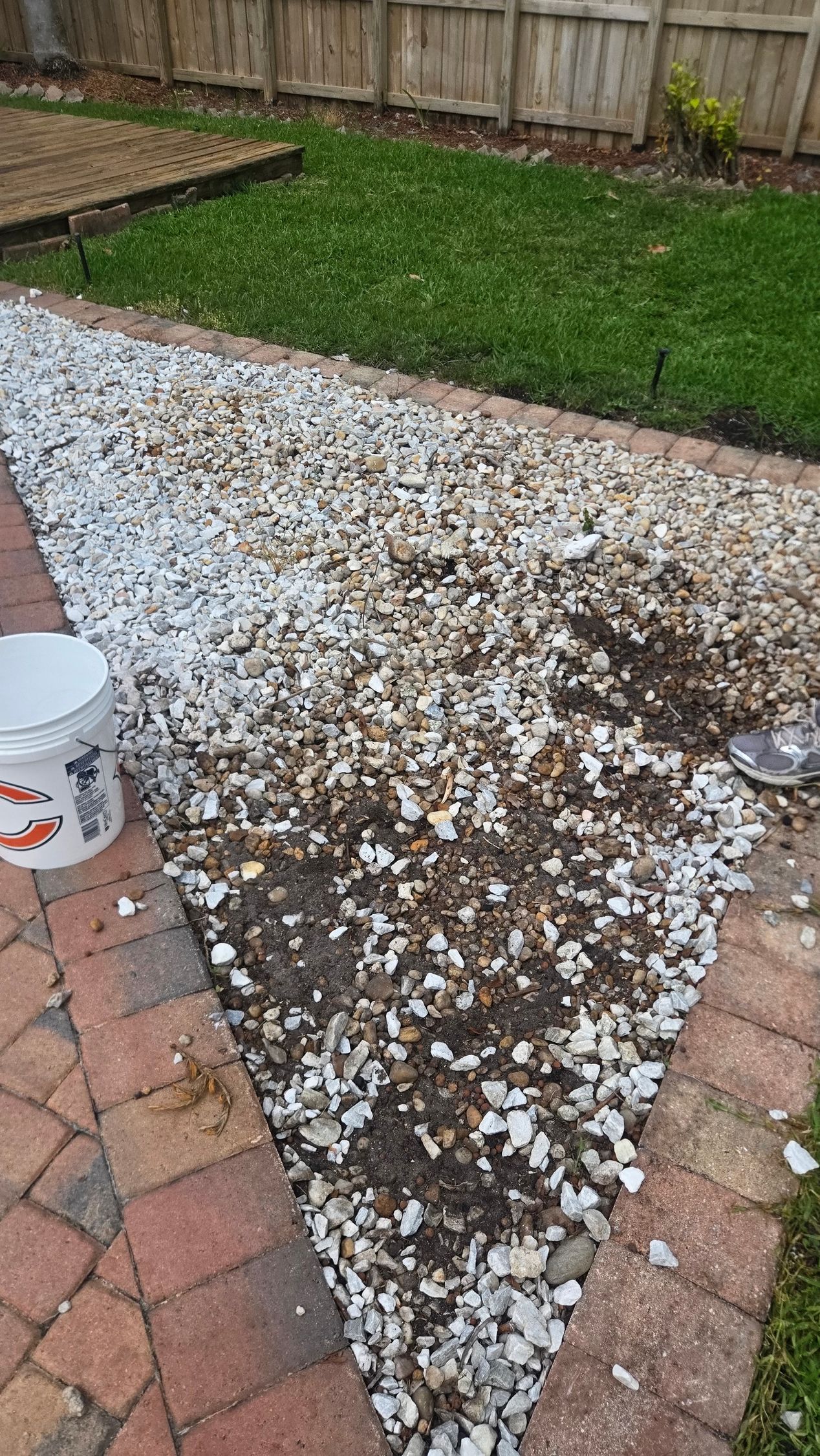 Triangular gravel patch between brick pavers and green lawn beside a wooden fence